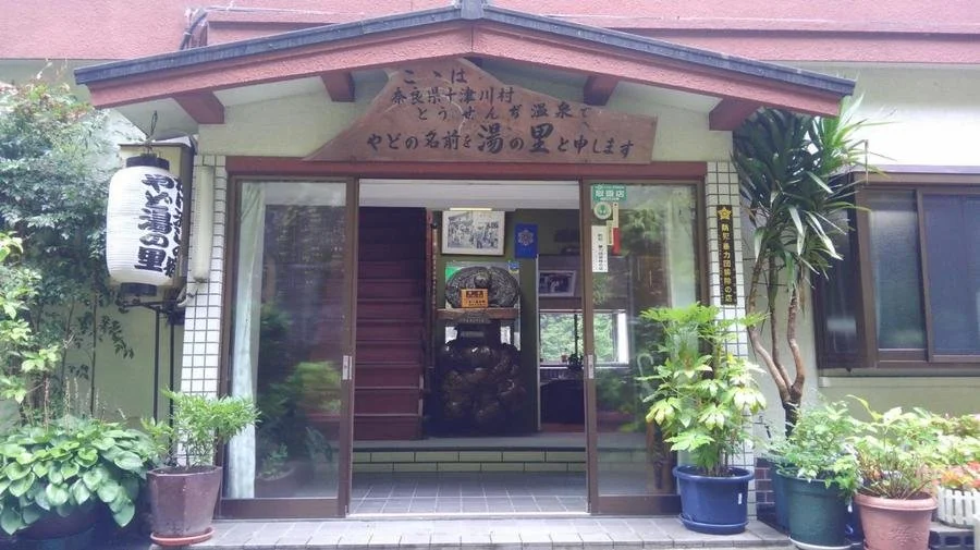 Entrance of Tousenji Onsen Yado Yunosato, a quiet seven-room mountain inn in Totsukawa Village, Nara, with white lantern and potted plants.