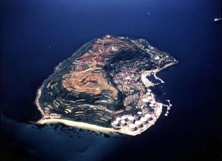 Aerial view of Mutsureshima, a small crab-shaped island near Shimonoseki with patchwork fields, a fishing village, and a historic lighthouse.