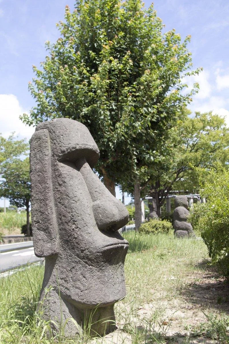 Replica moai statues standing in green grass along a former railway path at the Yane-no-Nai Roofless Museum in Nakama, Fukuoka.
