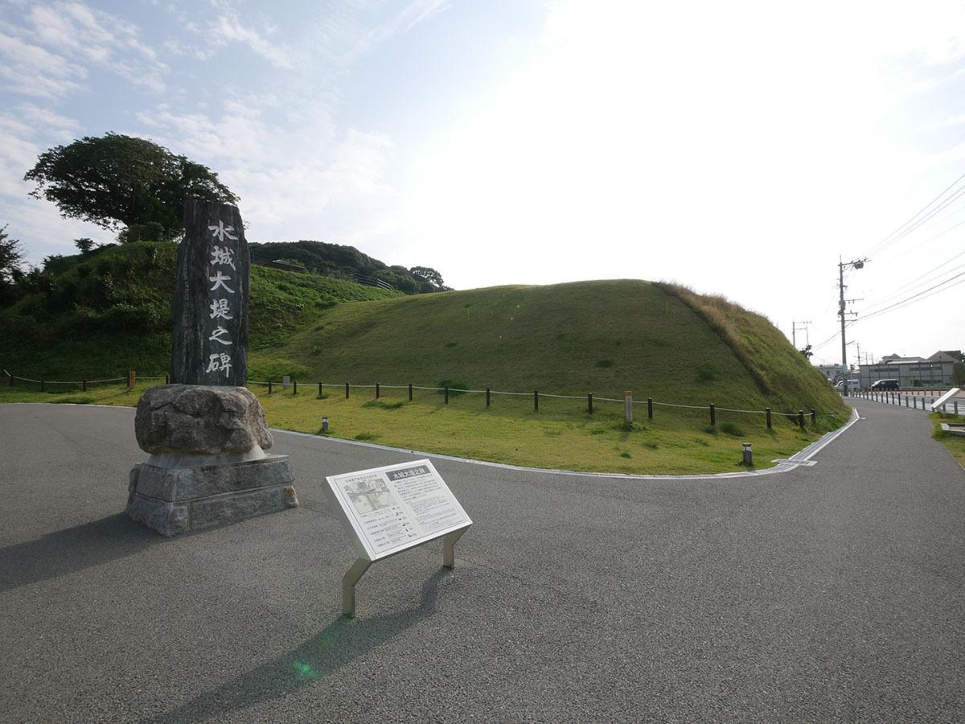 Stone monument and grassy earthen embankment of Mizuki Fortress ruins in Dazaifu — a 1,300-year-old defensive wall from ancient Japan.