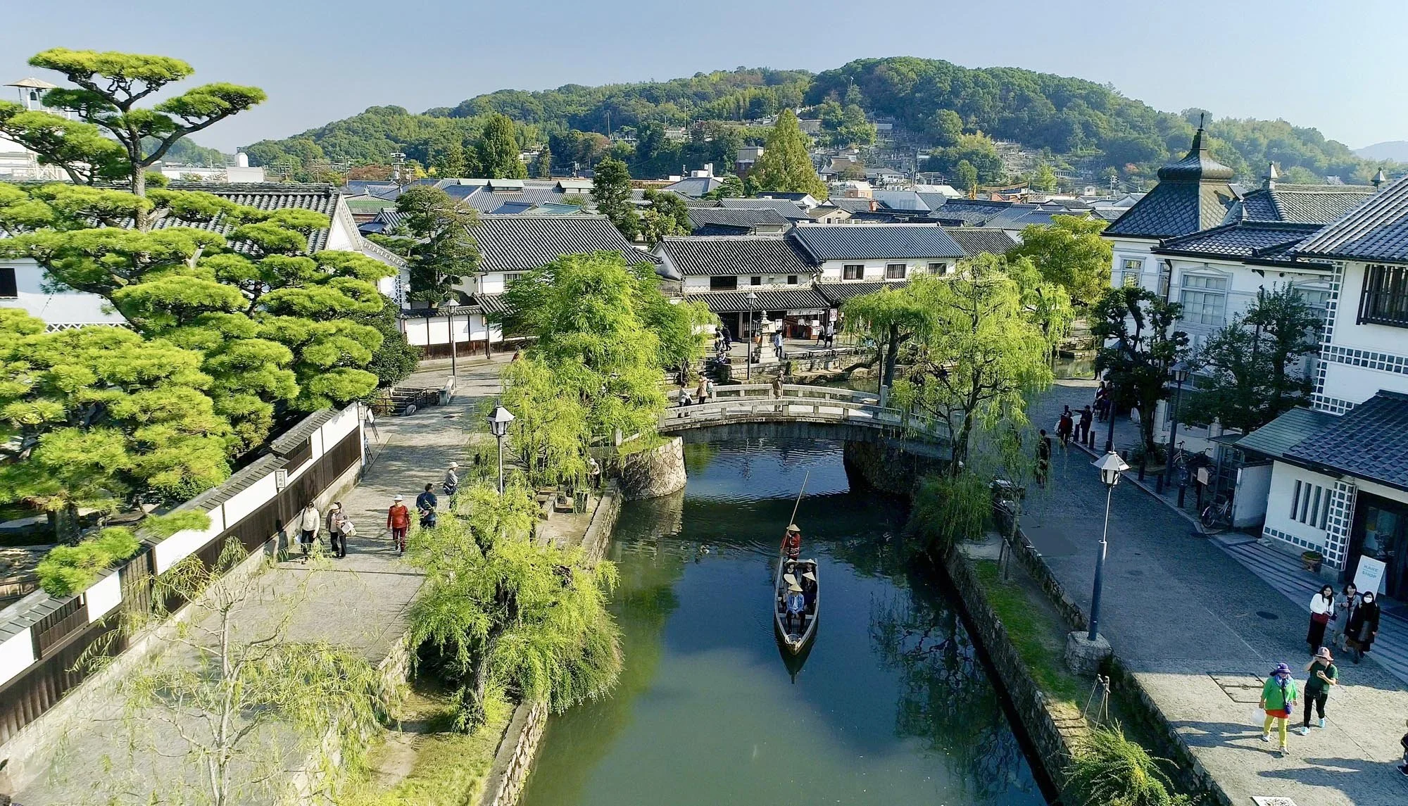 Kurashiki Bikan Historical Quarter — a traditional wooden boat glides along the willow-lined canal past white-walled storehouses in Okayama, Japan.