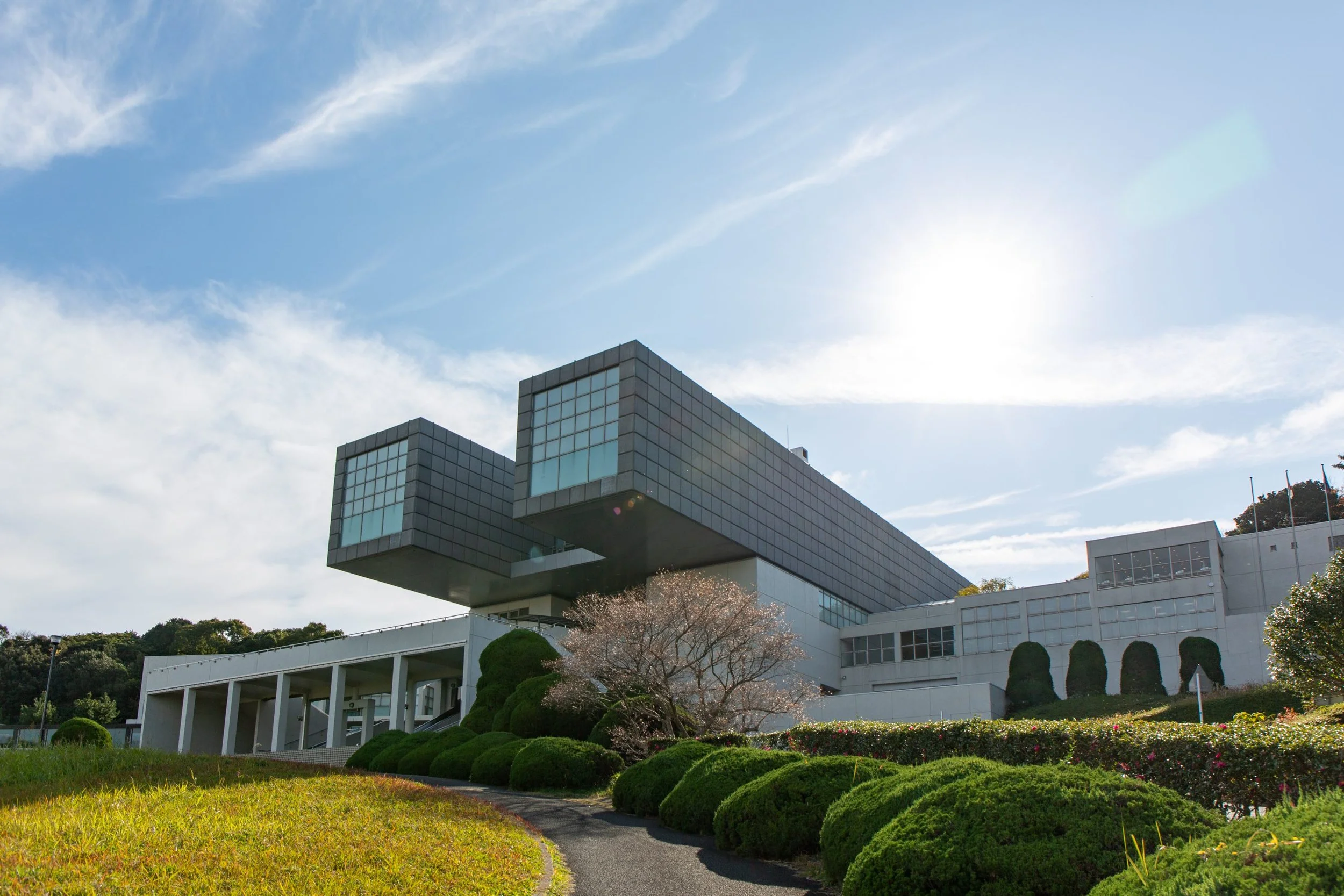 Kitakyushu Municipal Museum of Art by Arata Isozaki — twin cantilevered volumes rising above a green hilltop under a bright blue sky.