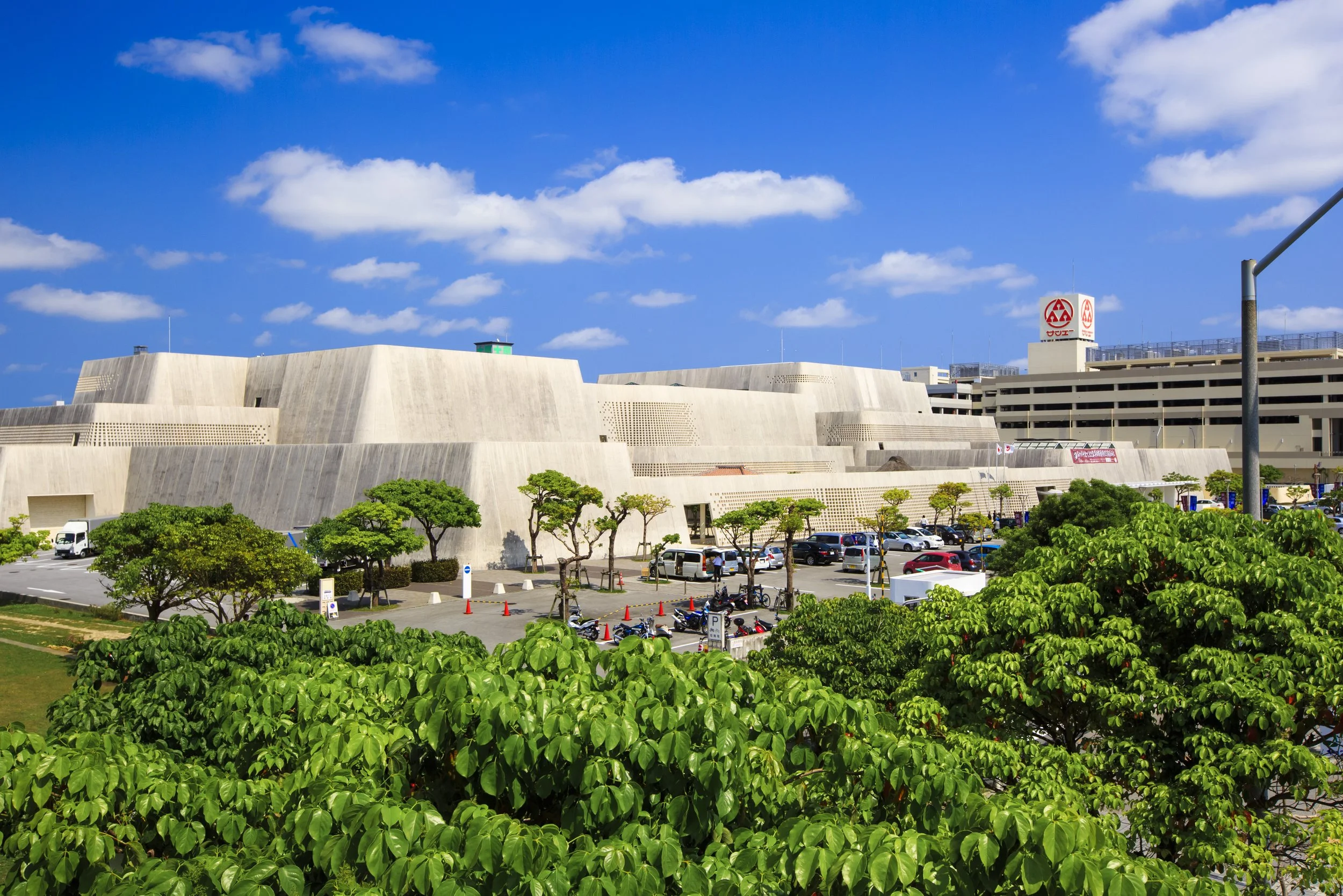 Okinawa Prefectural Museum's gusuku-inspired concrete facade under a vivid blue sky, surrounded by subtropical greenery in Naha.