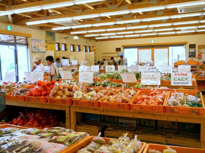 Locals browse orange crates of freshly harvested vegetables and garlic under wooden beams at Yotteko Shikisai-kan, a farm stand in Miyako Town, Fukuoka.
