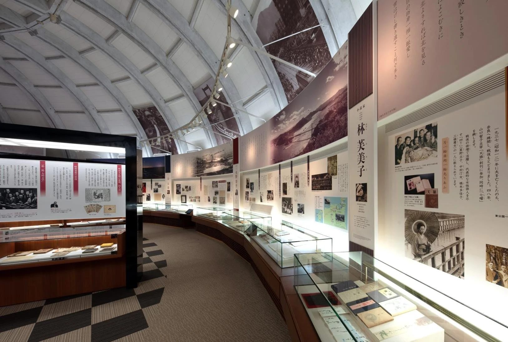 Curved vaulted gallery of the Kitakyushu Literature Museum with illuminated display panels and glass cases showcasing rare Japanese literary materials.