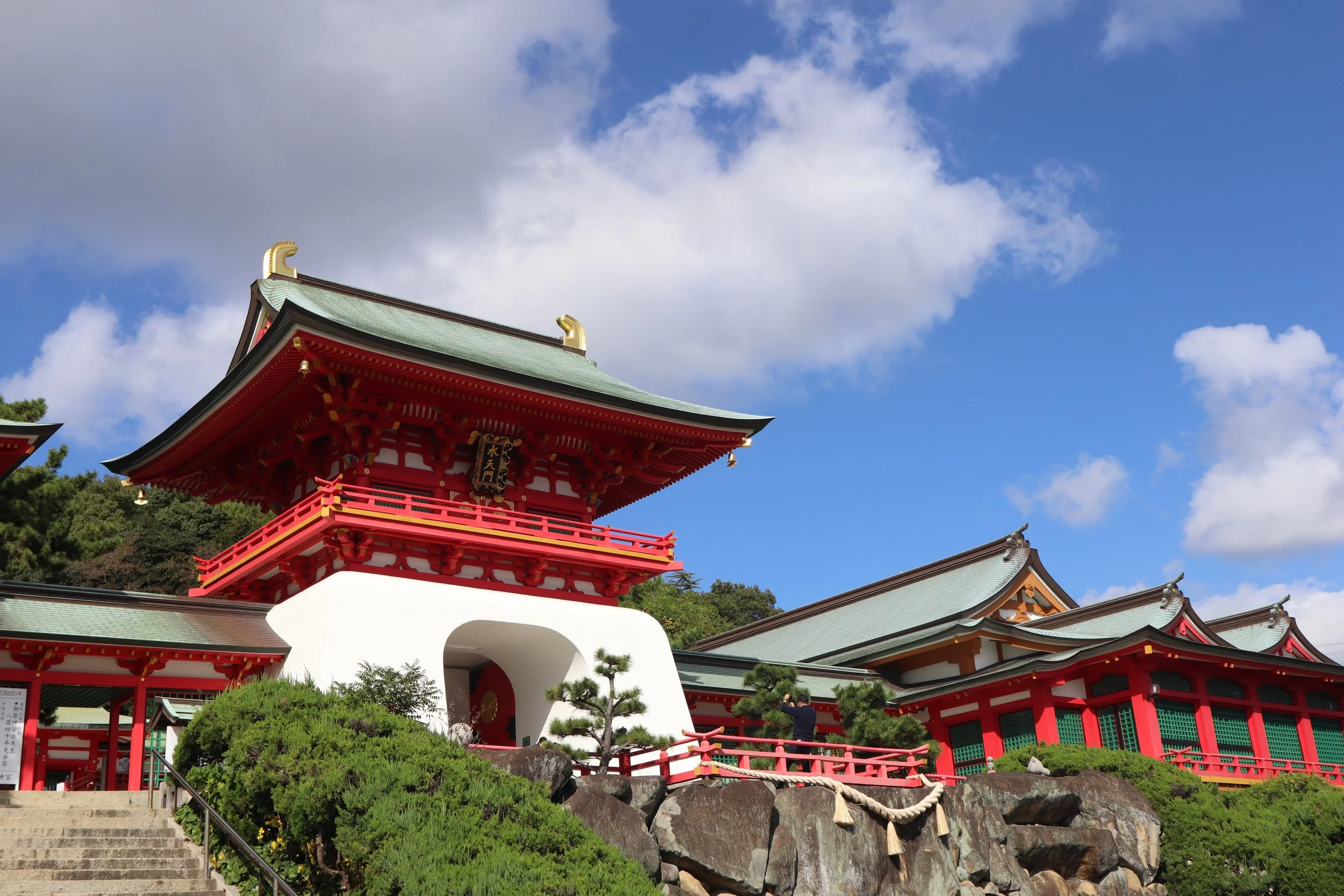The vermilion Suitenmon gate of Akama Shrine in Shimonoseki, with green-tiled curved roofs against a bright blue sky — a memorial to the Heike clan.