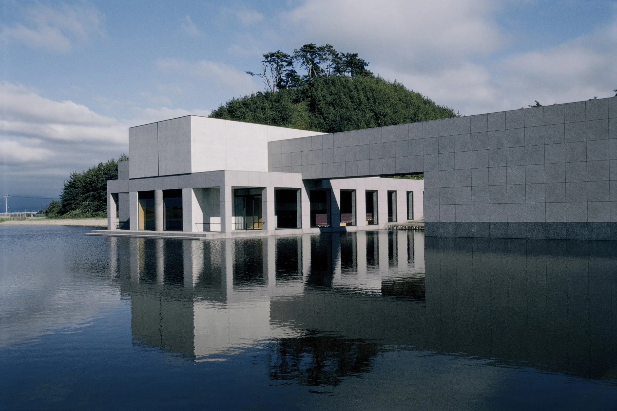 Ken Domon Museum of Photography reflected in a still pond at Iimoriyama Park, Sakata — a masterpiece of Japanese architecture and slow travel.