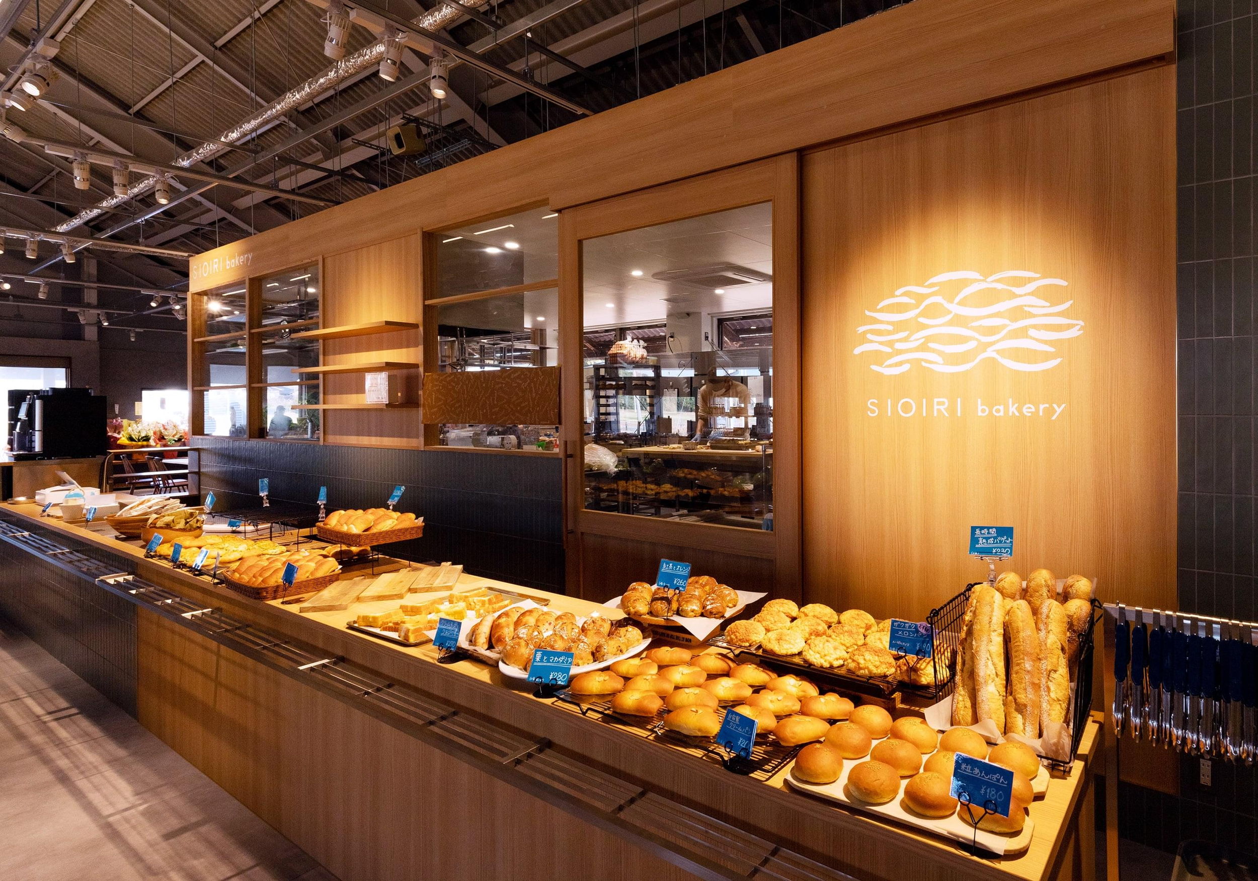 A modern building with glass doors and windows, decorated with flags and signs, including a cartoon tiger mascot wearing a white hat and cape, outdoors on a sunny day with trees in the background.