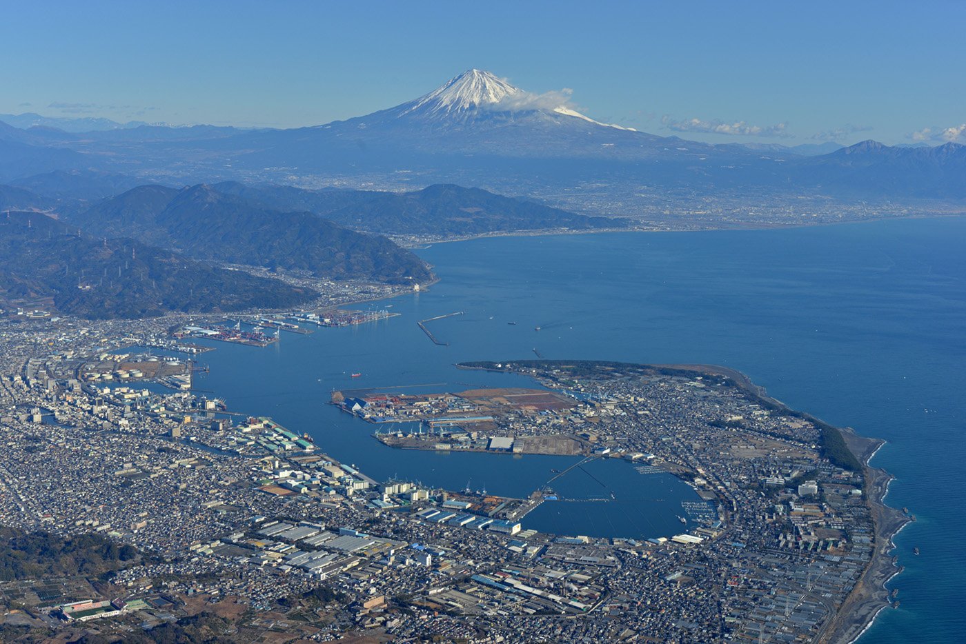 Aerial view of Shimizu Port in Shizuoka with the snow-capped Mount Fuji rising above the bay and harbor landscape.