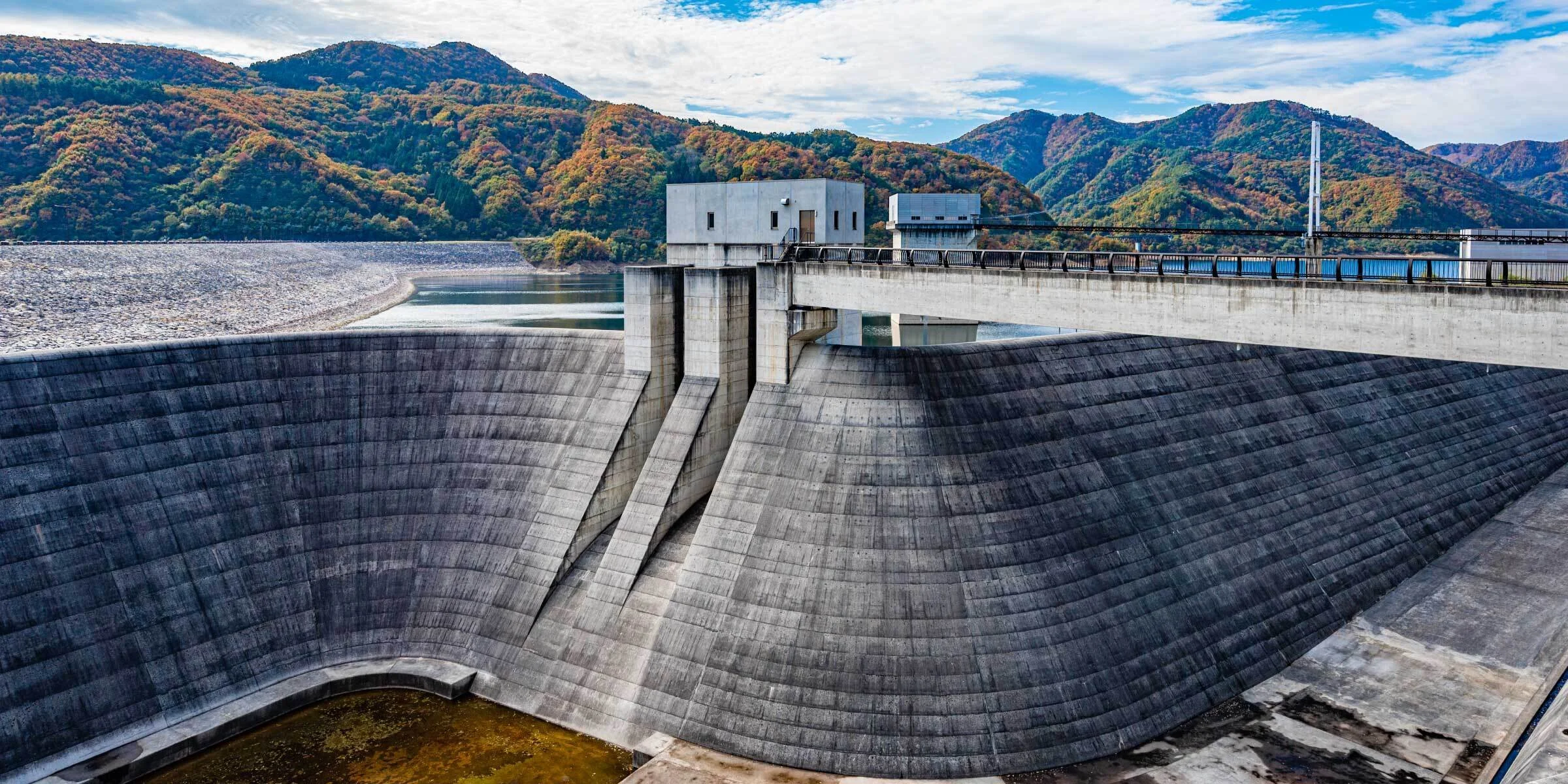 Surikamigawa Dam in autumn — a sweeping concrete dam framed by crimson and gold forested hills in Fukushima, Japan.