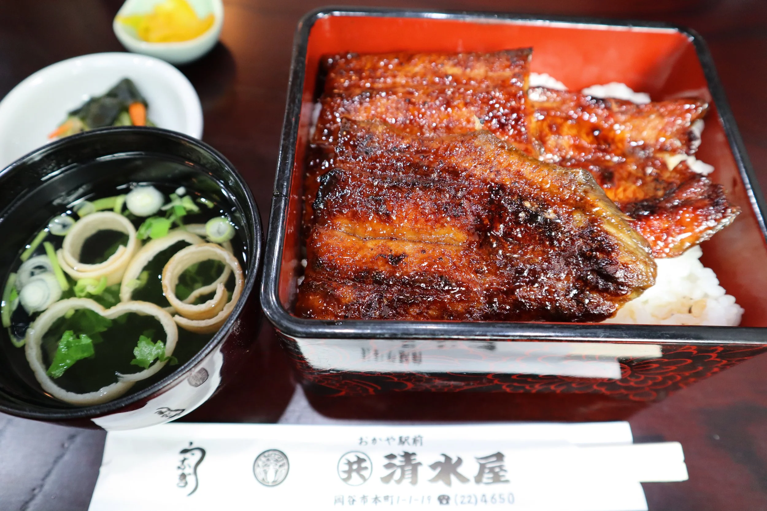 Glossy grilled unagi over rice in a lacquered box with clear broth and pickles at Shimizuya, a specialty eel restaurant in Okaya, Nagano.