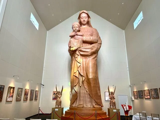 Towering 10-meter wooden Virgin Mary statue flanked by carved angels inside the softly lit Harajo St. Mary's Kannon Hall in Nagasaki.