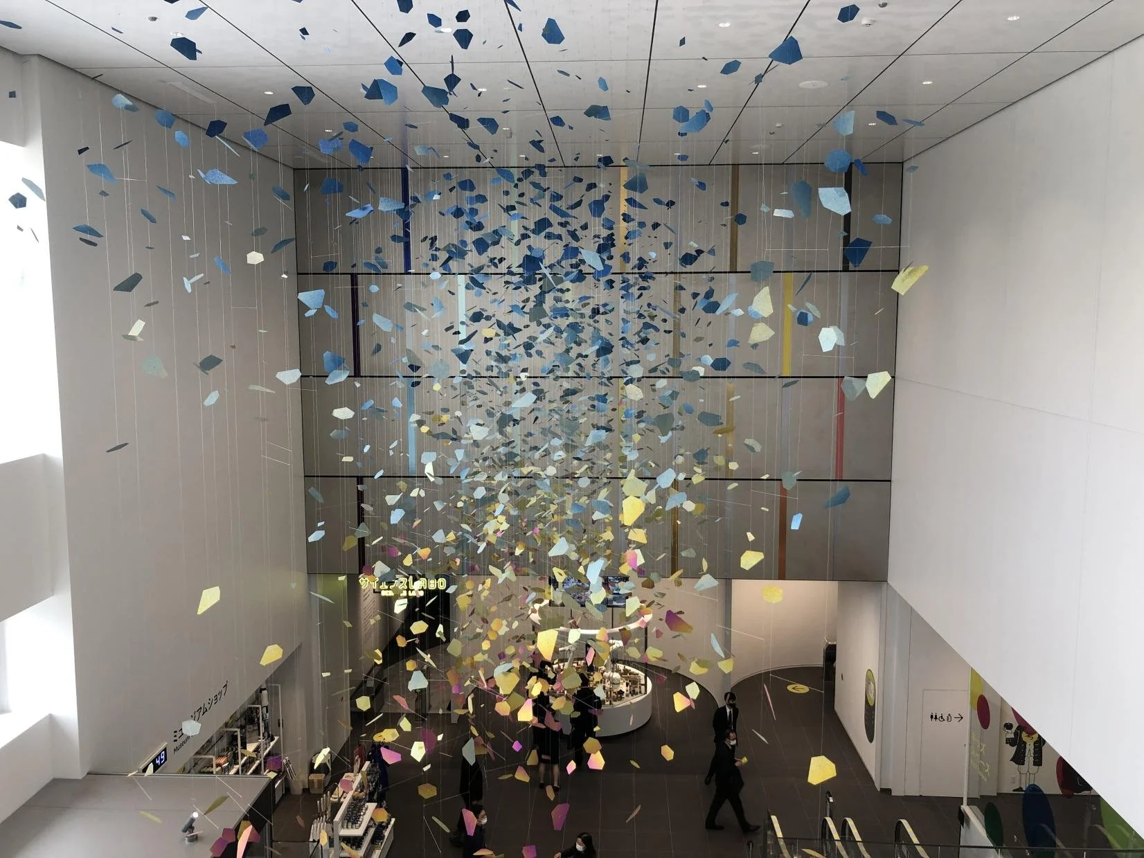 Suspended colorful kinetic art installation cascading through the bright atrium entrance of Space LABO science museum in Kitakyushu, Japan.