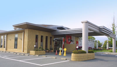 A modern fast food restaurant with a yellow brick exterior, a large canopy entrance, and a parking lot in front.