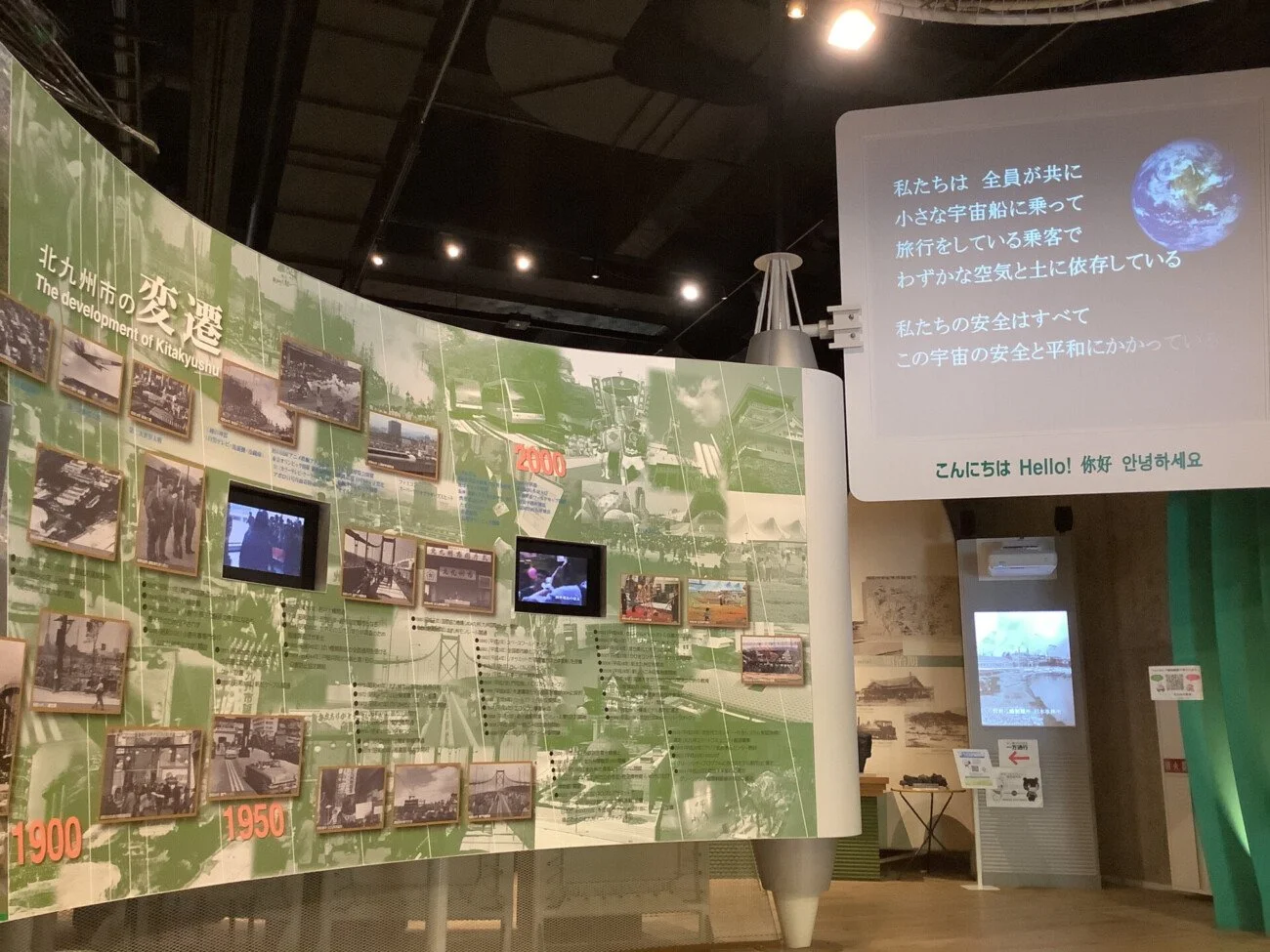 Curved green exhibit wall with timelines and photos at Takamiya Environmental Museum, showing Kitakyushu's journey from industry to sustainability.