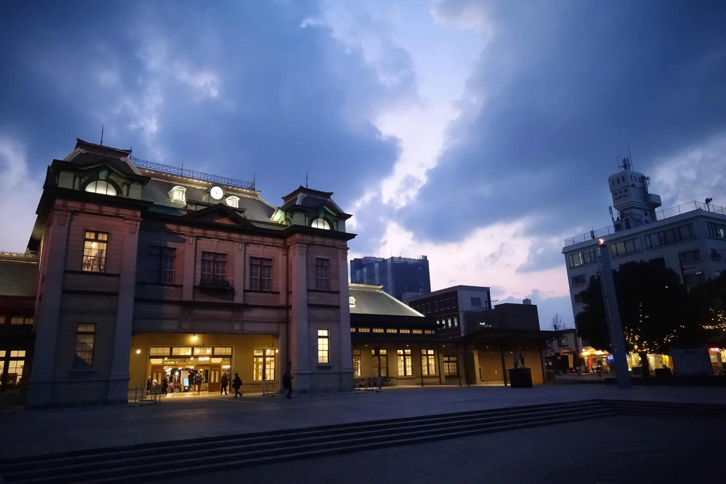 Mojiko Station illuminated at dusk, its historic retro façade glowing against a blue twilight sky in Kitakyushu, Japan.