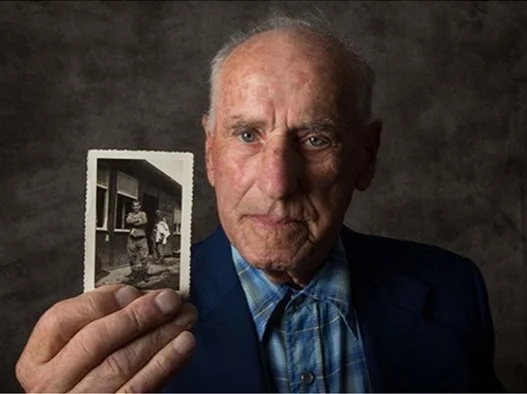 Elderly Jewish man holding an old photograph of himself as a young man