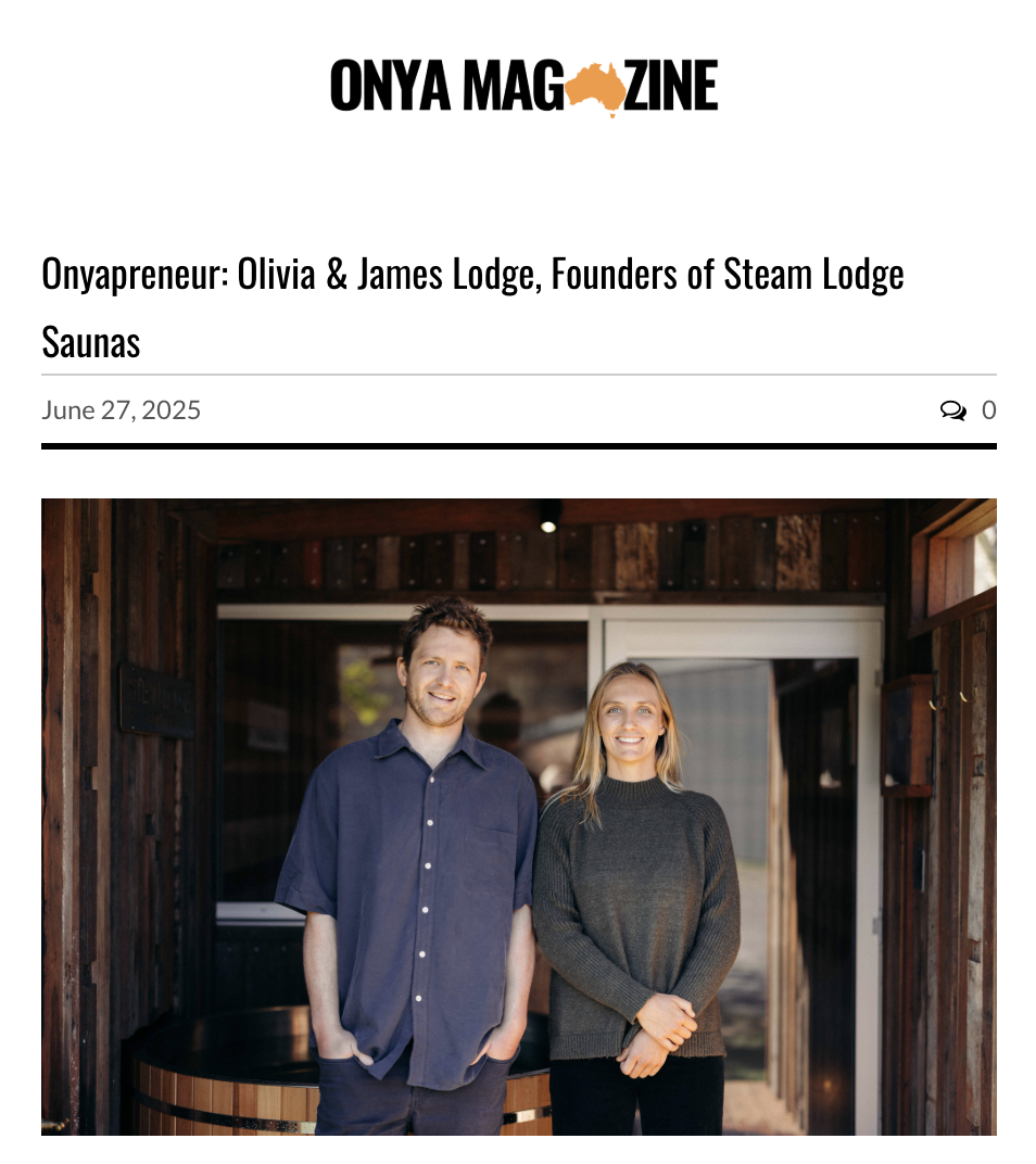 A man and woman standing outside a wooden sauna building, smiling at the camera.