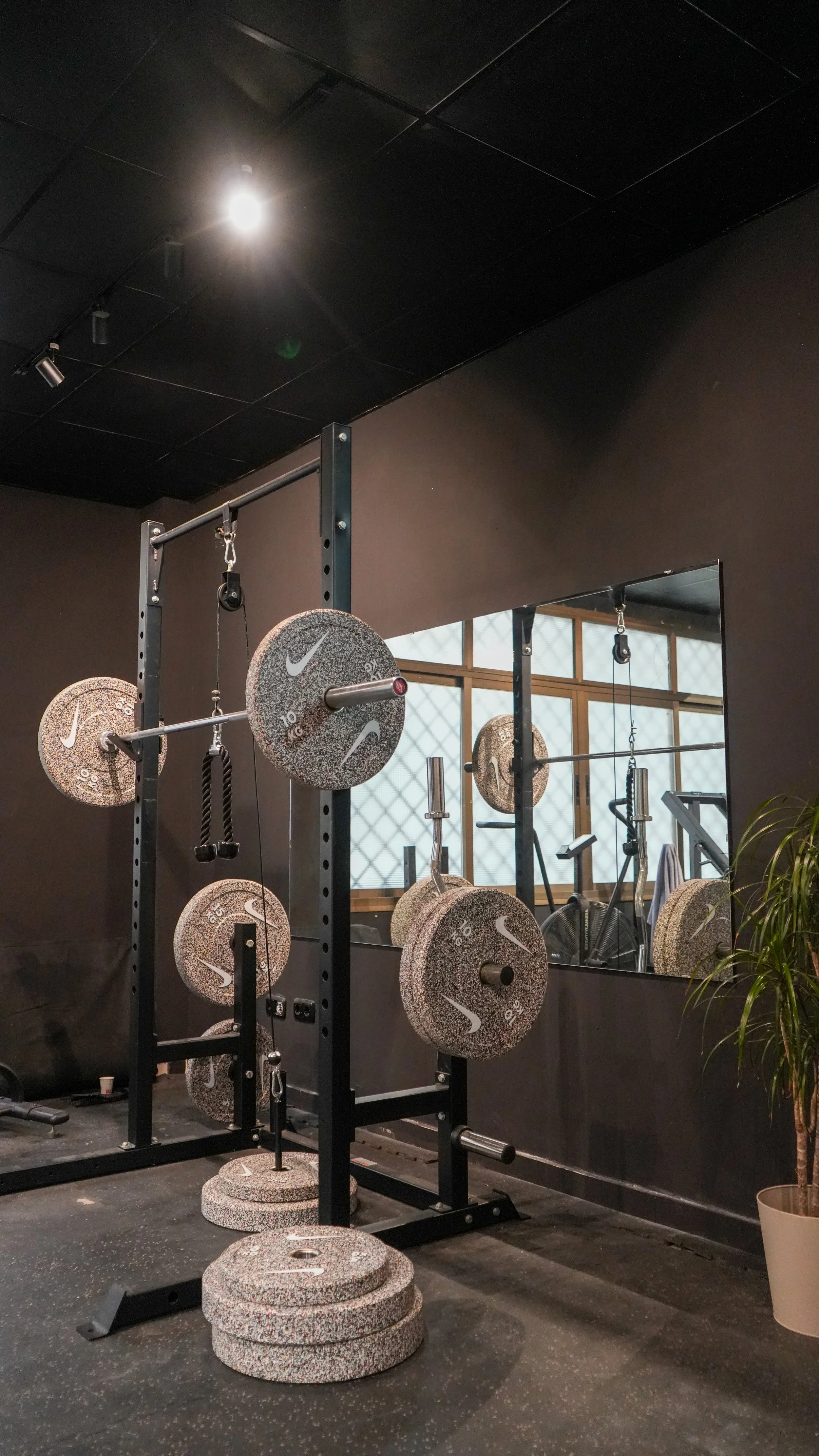 Equipo de pesas en un gimnasio, incluyendo pesas de diferentes tamaños y una barra con peso, reflejado en un espejo.