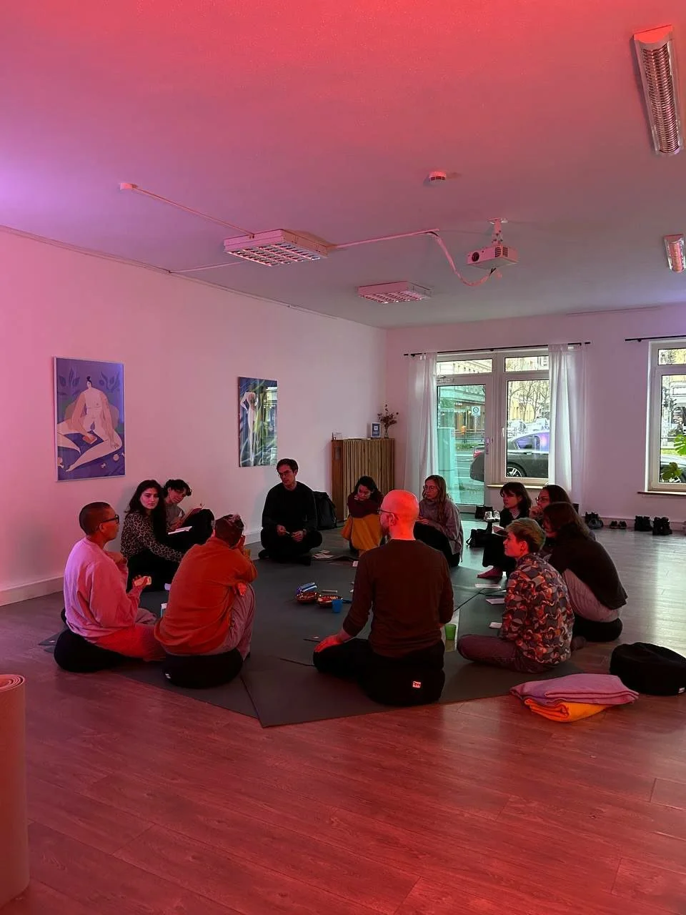 A group of people sitting in a circle in a room with cosy pink lighting