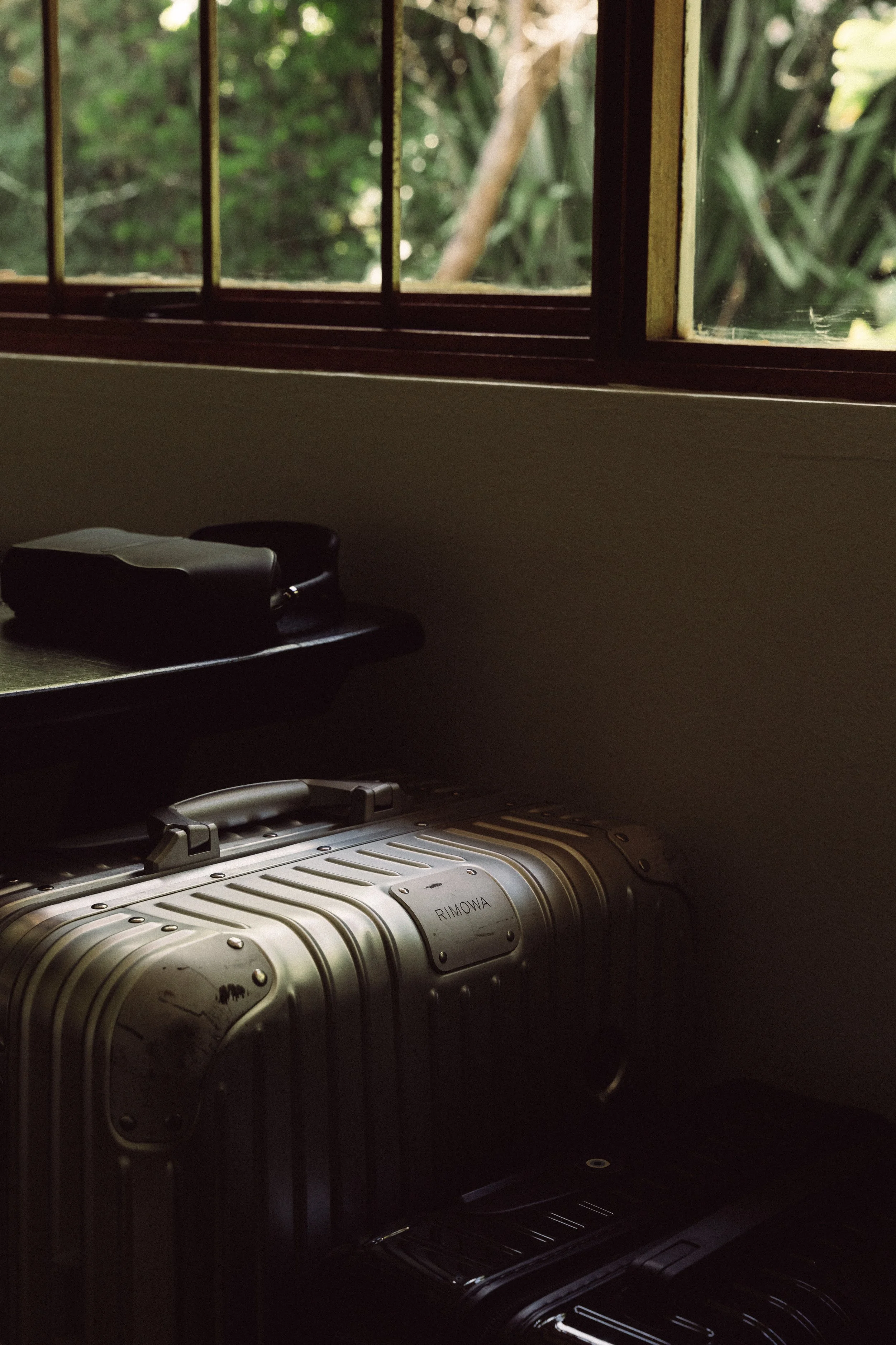 Koffer und Taschen auf einem Boden neben einem Fenster mit Blick ins Grüne.