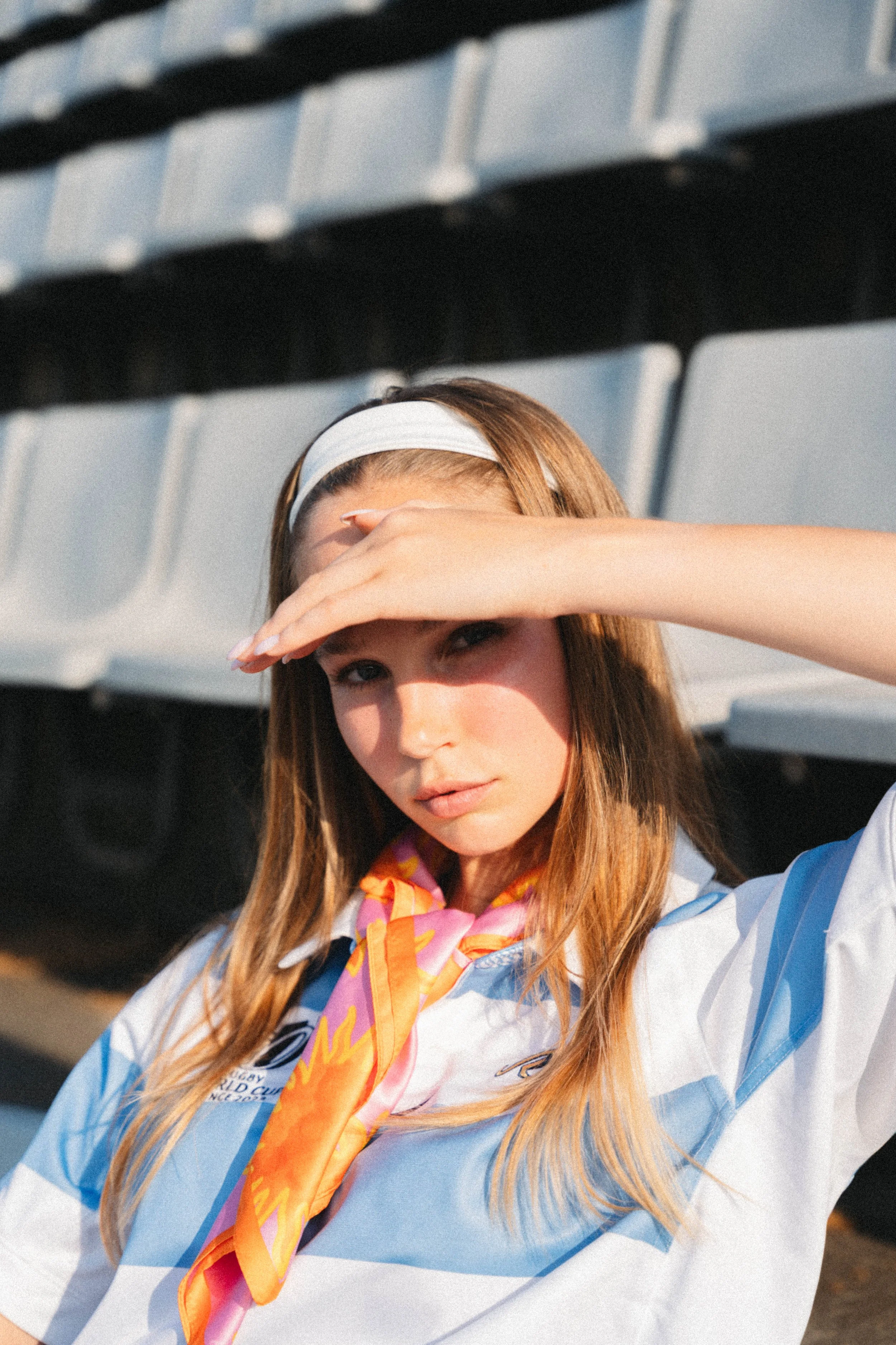 Junge Frau in Rennteam-Uniform mit Sonnenbrille, Sonnenlicht auf der Stirn, sitzt auf Tribüne.