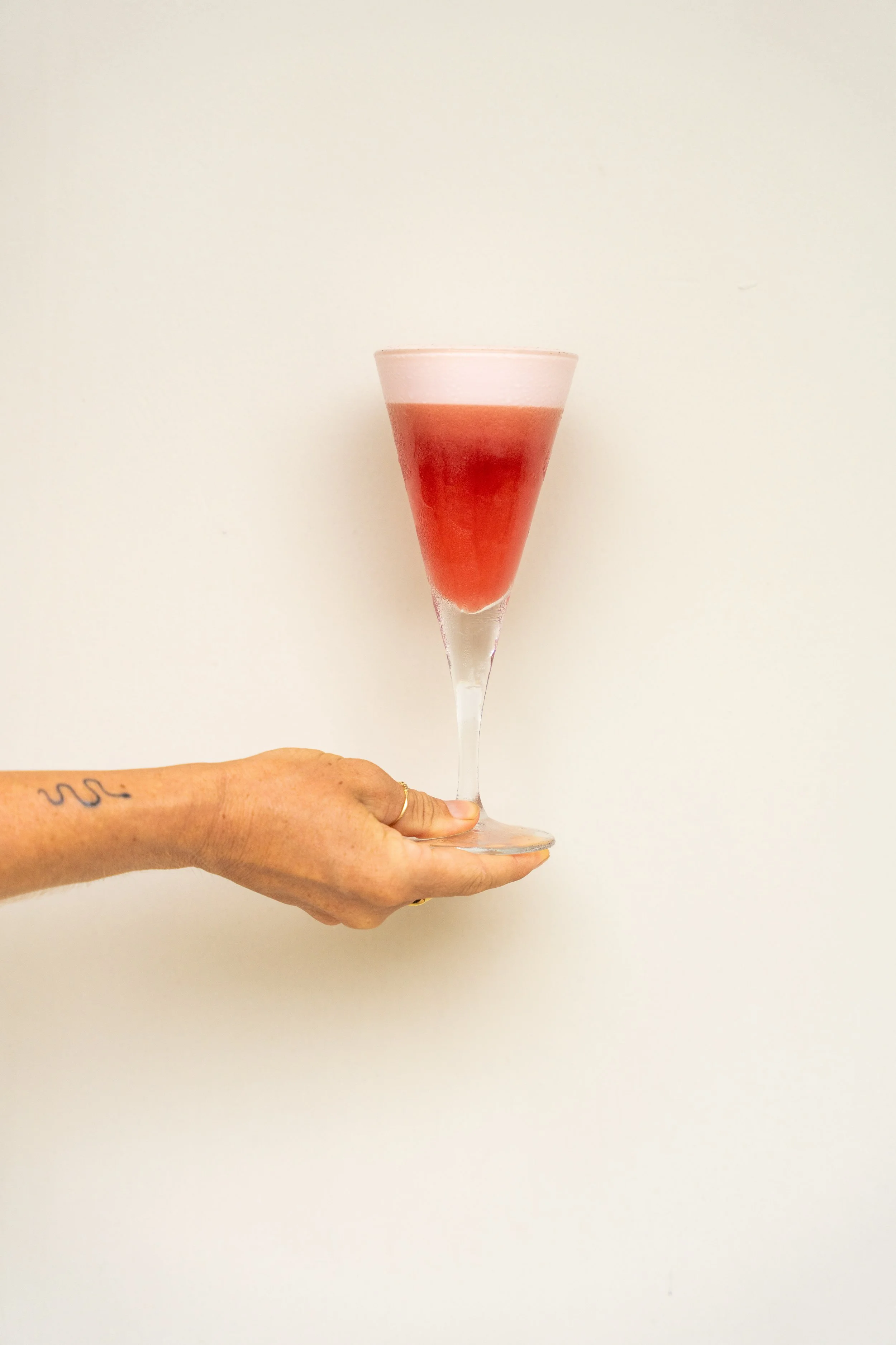 Hand hält einen Cocktail im Sektglas gegen weißen Hintergrund.