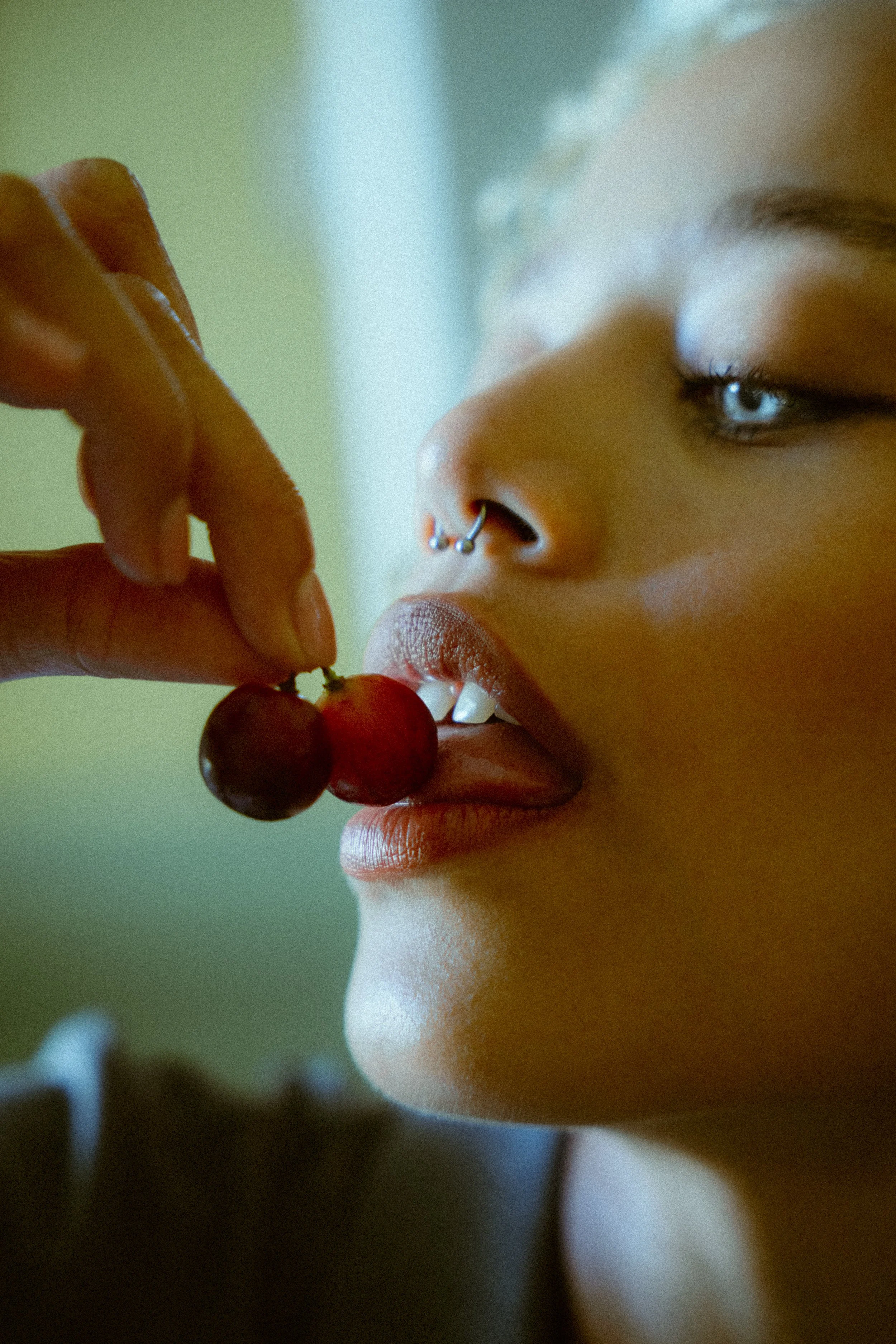 Nahaufnahme eines jungen Mädchens mit Nasenring, das eine Traube isst, ihre Zunge ist leicht ausgefahren und sie hat blaue Augen.