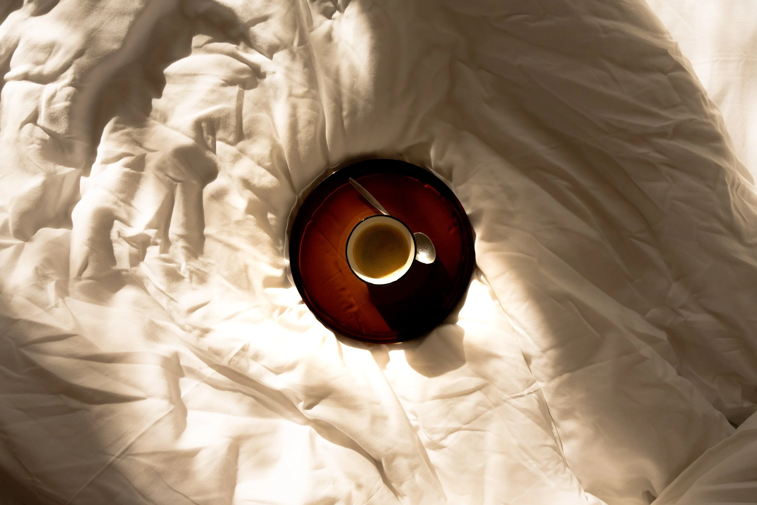 Tasse Tee auf rotem Tablett, platziert auf weißer, zerknitterter Bettwäsche, aufgenommen von oben.