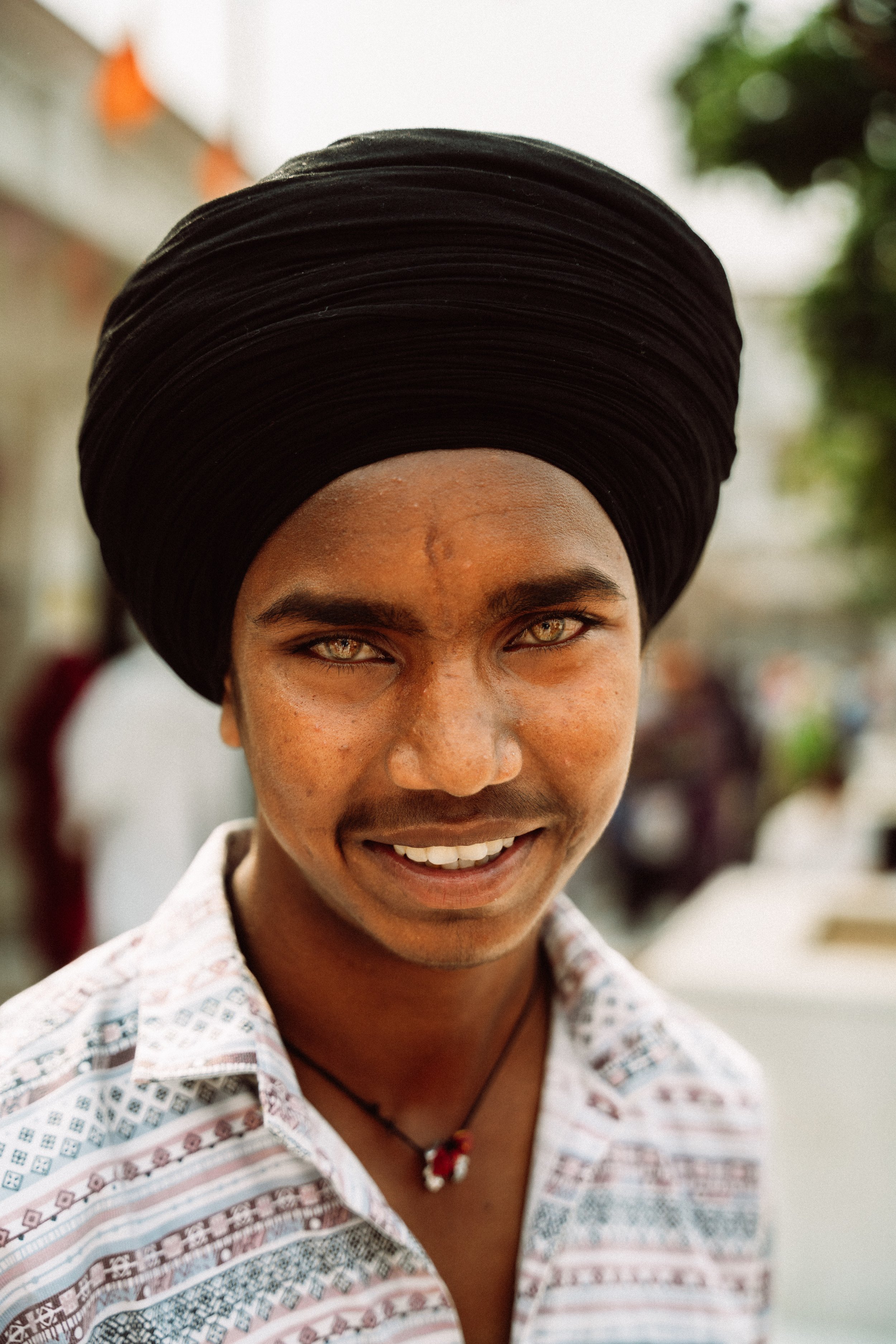 Nahaufnahme eines lachenden Mannes mit dunklem Turban und hellem Hemd im Freien.