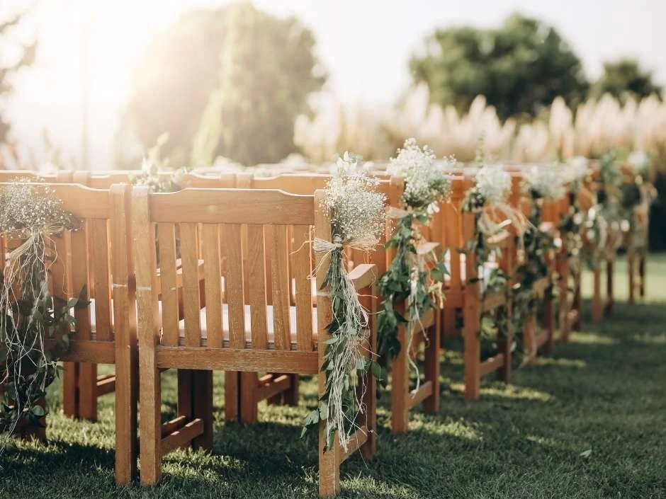 Wooden bench seating with eucalyptus and baby's breath aisle markers at a sunlit outdoor wedding ceremony