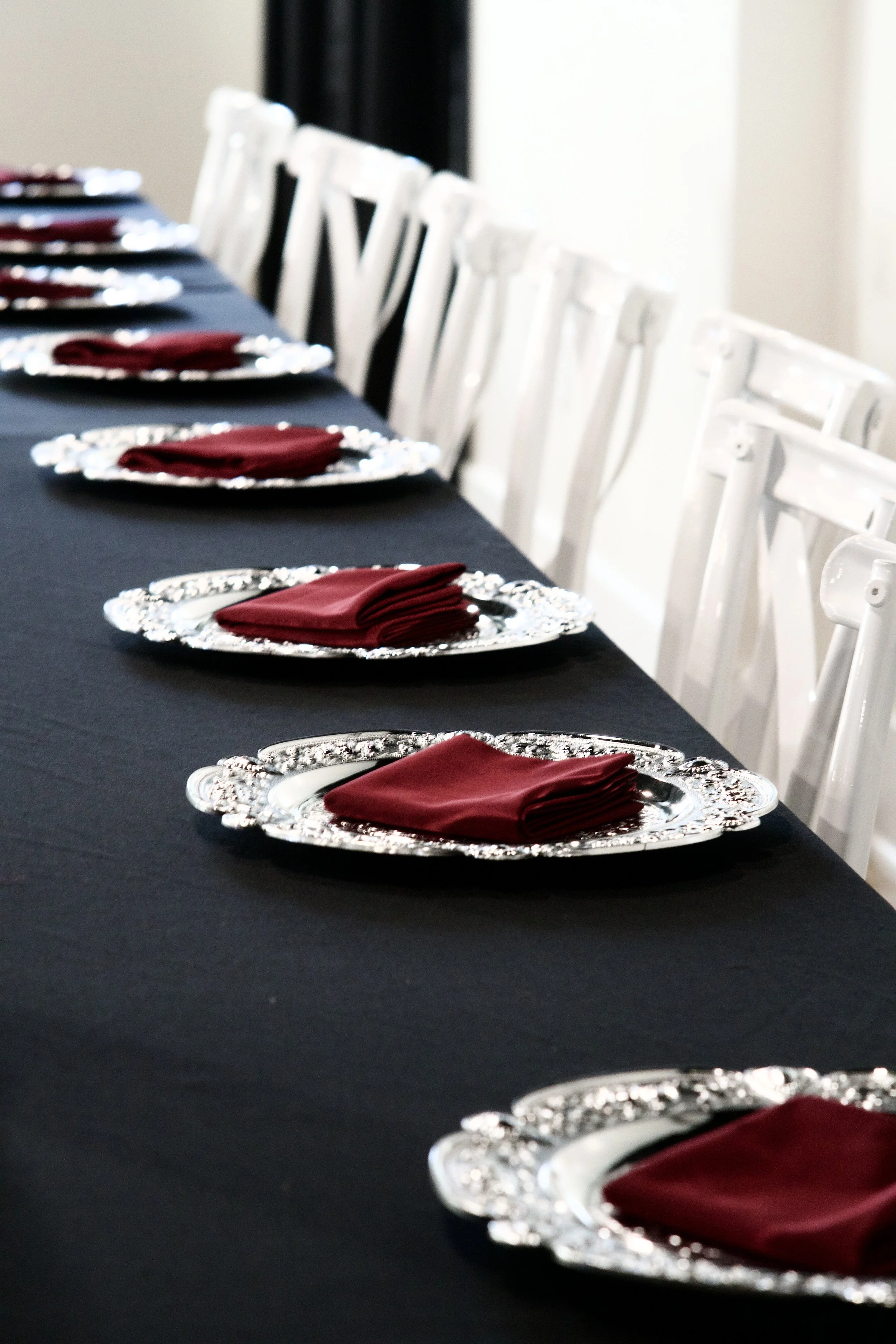 row of silver chargers with burgundy napkins along a black reception table