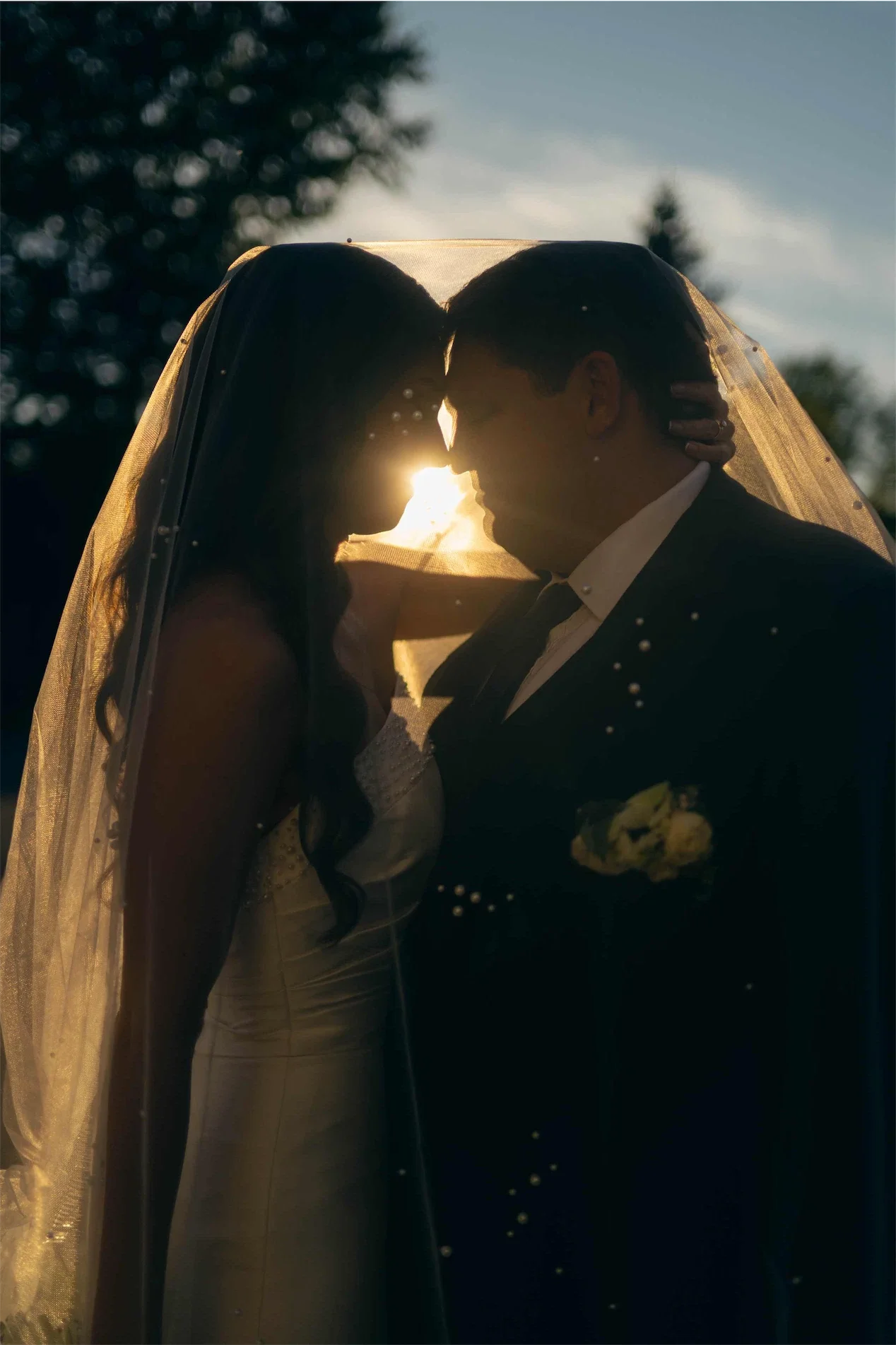 sunset-silhouette-couple-under-veil-foreheads-touching.webp
