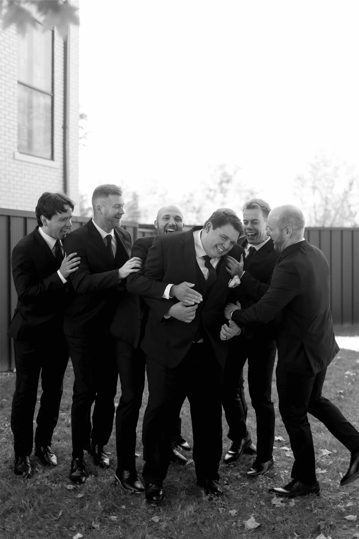 groomsmen-laughing-around-groom-black-and-white.webp