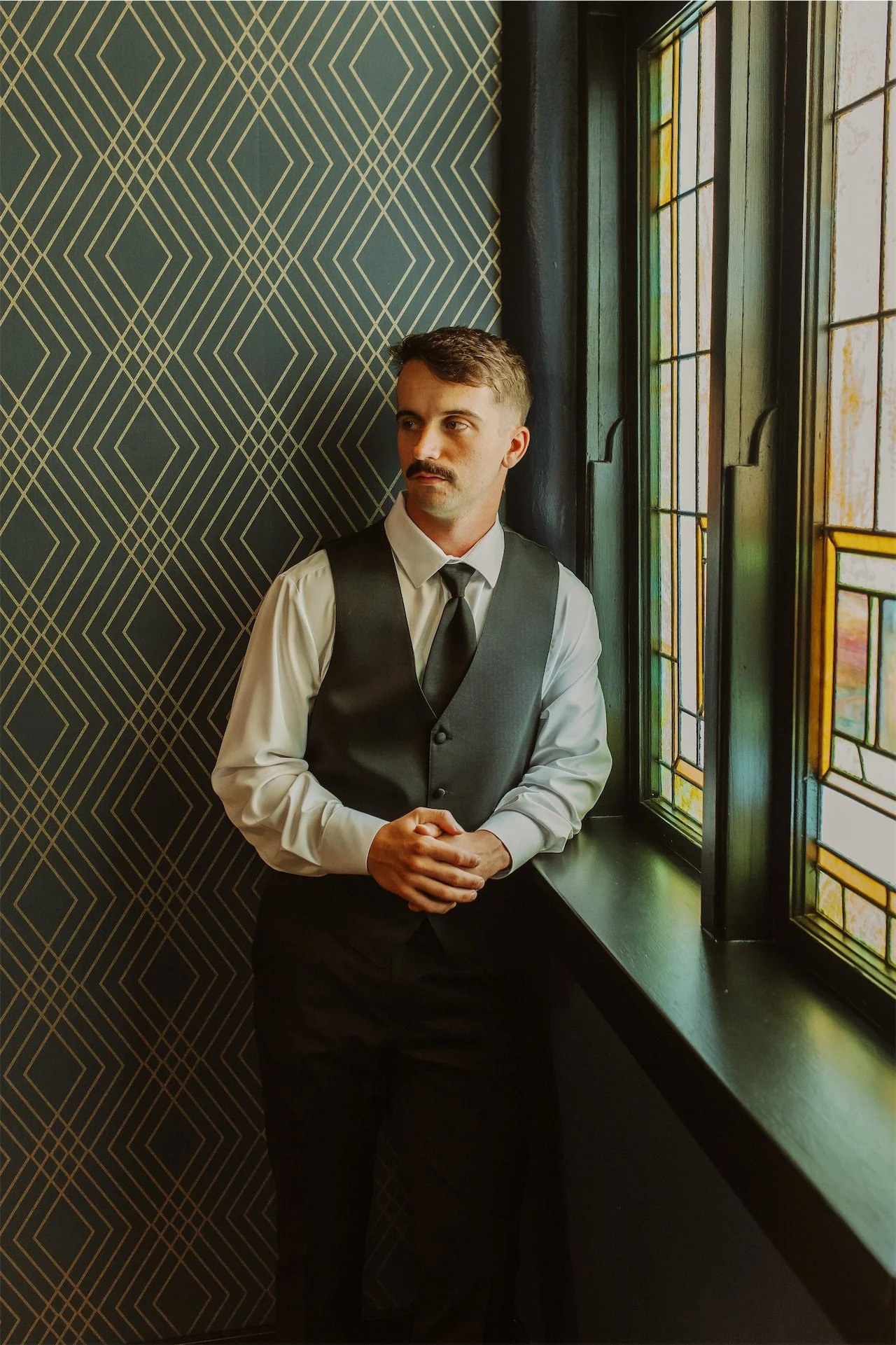 Groom in vest and tie standing beside stained glass window at church venue