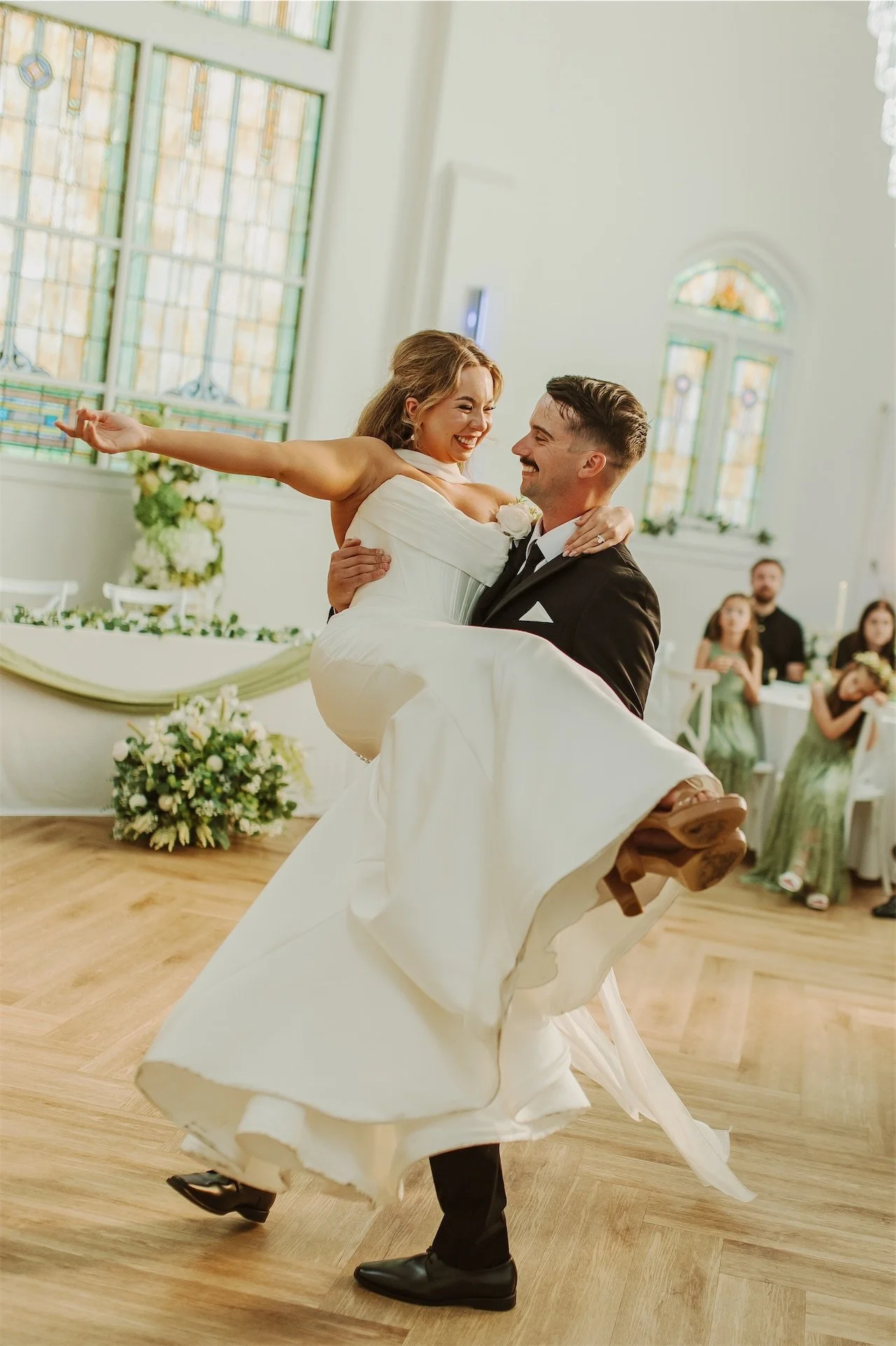 Bride twirling with groom during first dance beneath stained glass windows