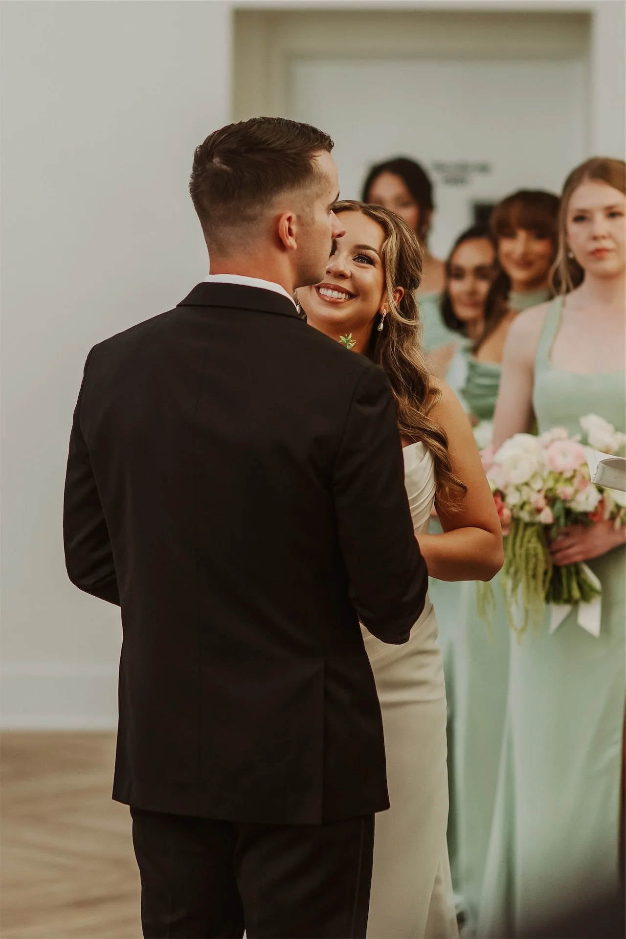 Bride and groom facing each other during vows with bridesmaids in sage green