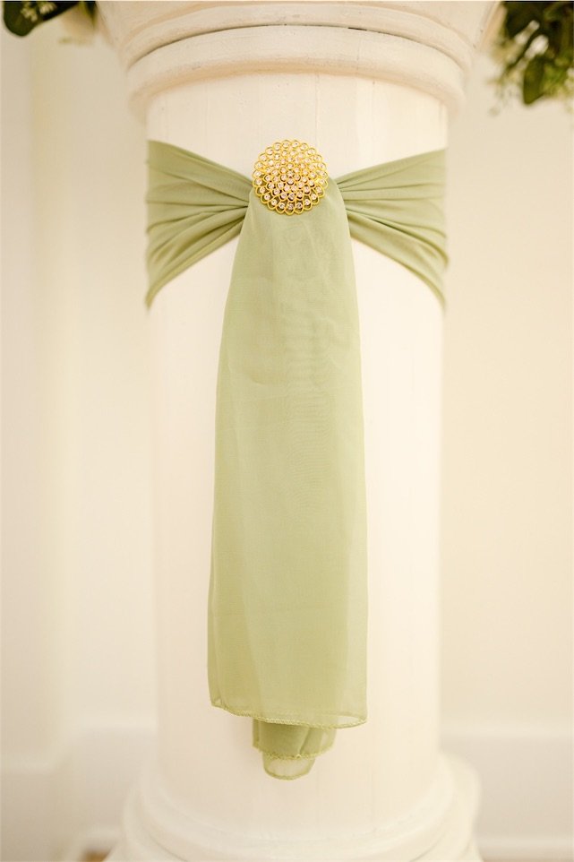Sage green chiffon sash tied around a white column with a gold brooch