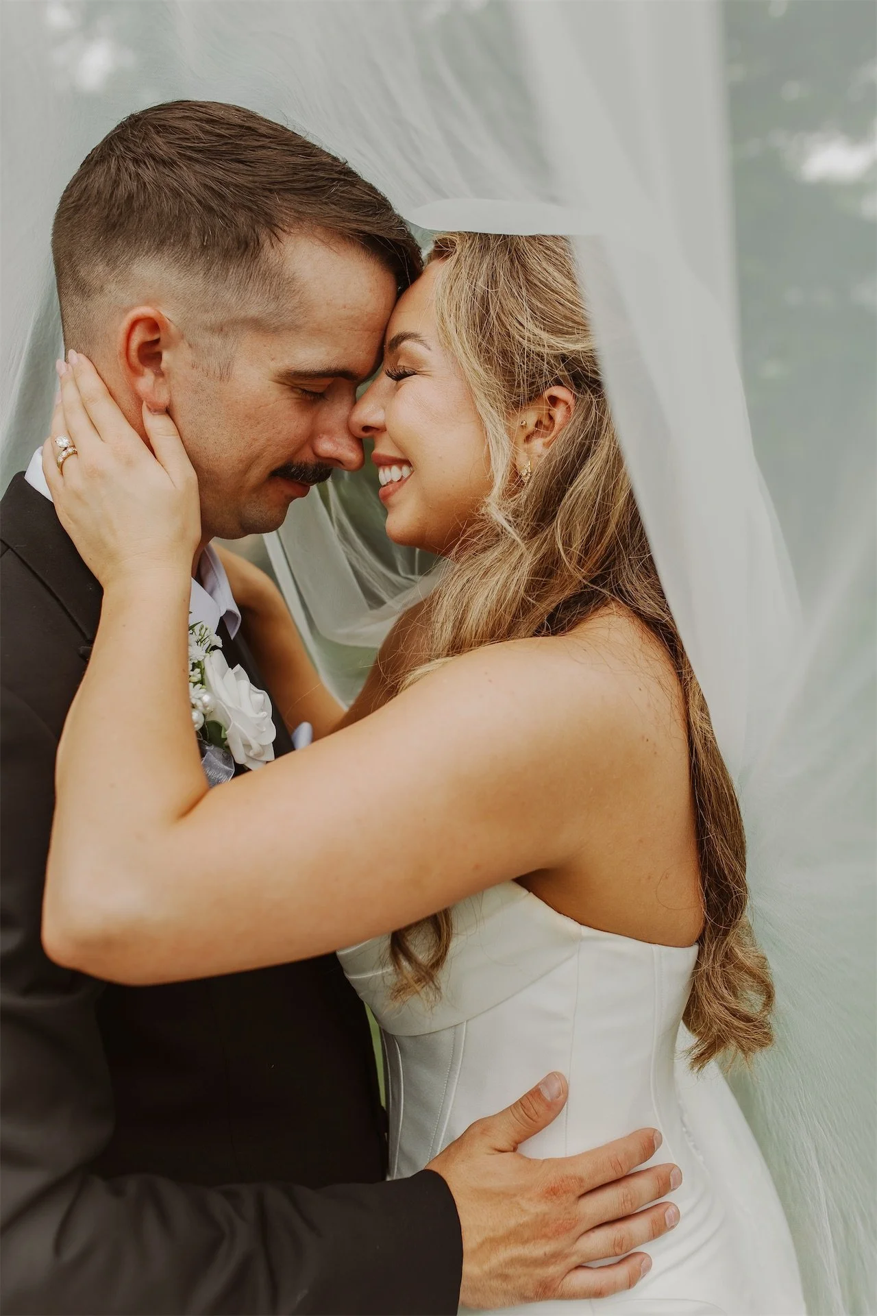 Bride and groom embracing forehead to forehead under cathedral veil
