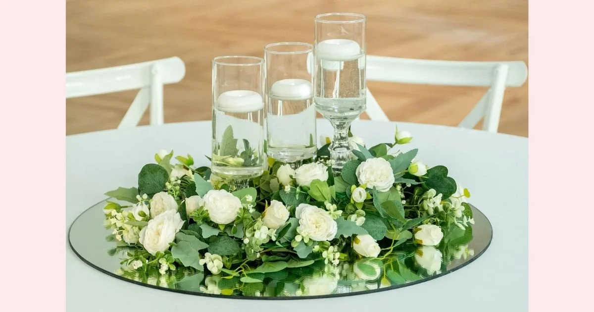 mirrored centerpiece with floating candles surrounded by white roses and greenery