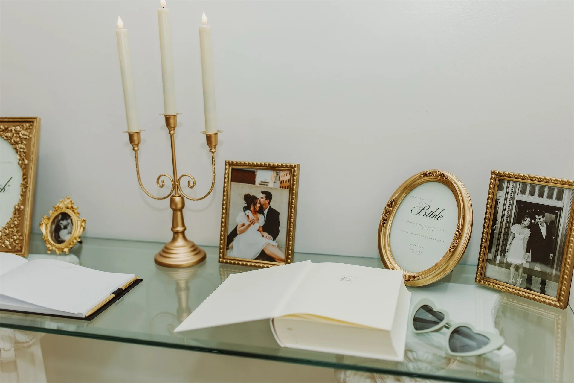 Wedding guest book and gold frames styled on glass table at reception