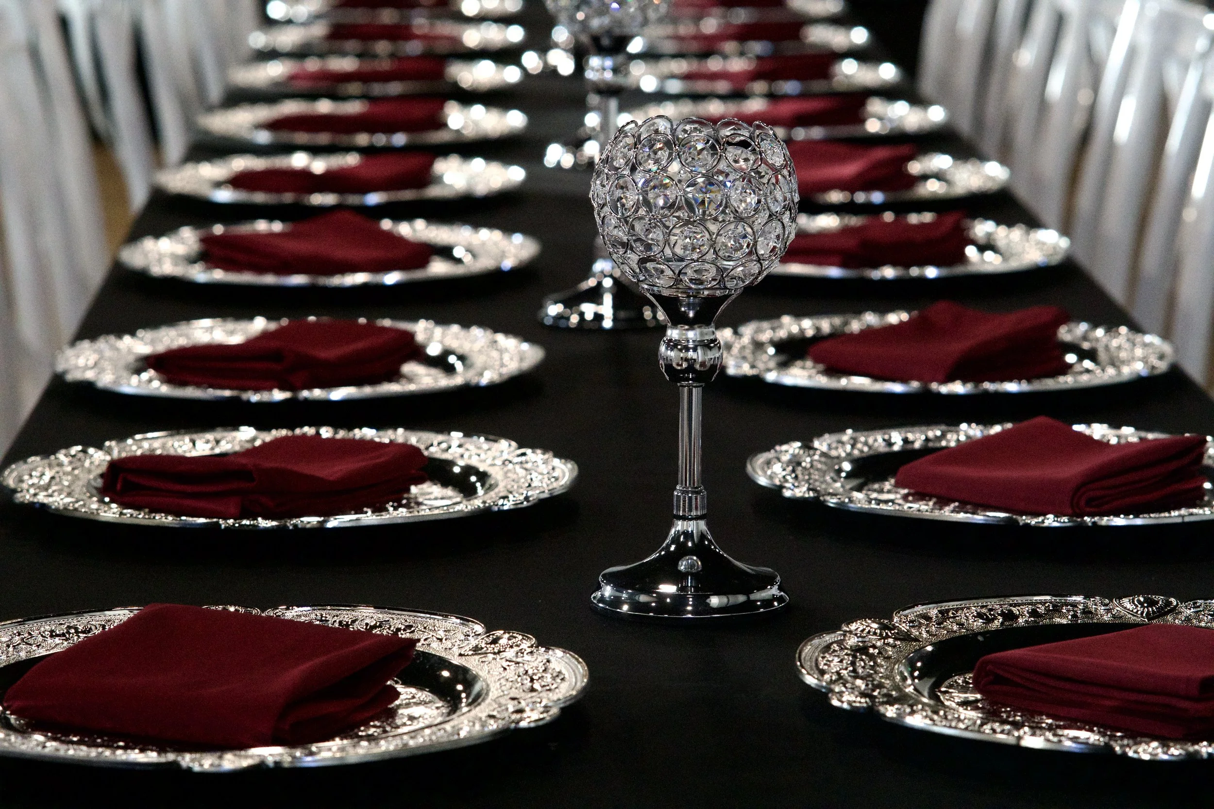 crystal goblet centerpiece rising above a row of burgundy napkin place settings