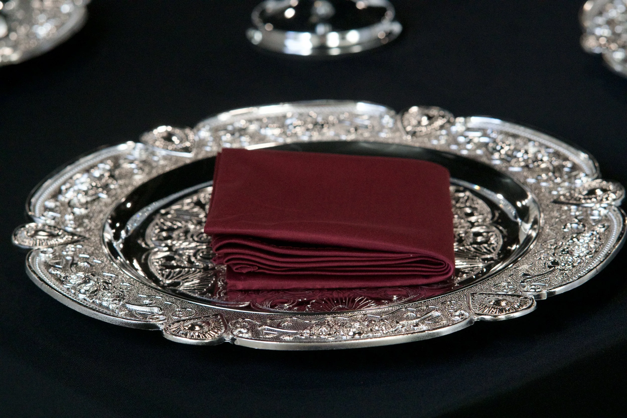 close detail of burgundy folded napkins on ornate silver charger plates