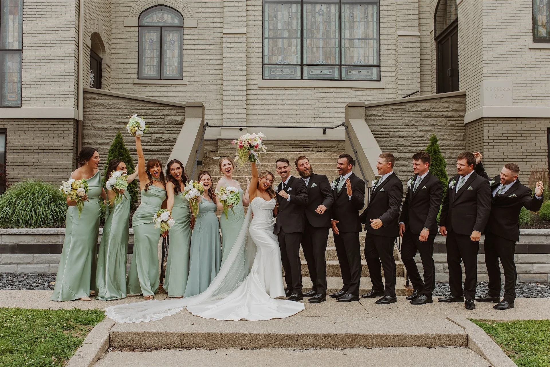 Wedding party cheering outside historic church with bridesmaids in sage green dresses
