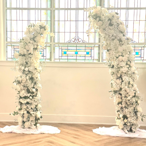 white cascading floral columns standing beneath a Kaleidoscope stained glass window