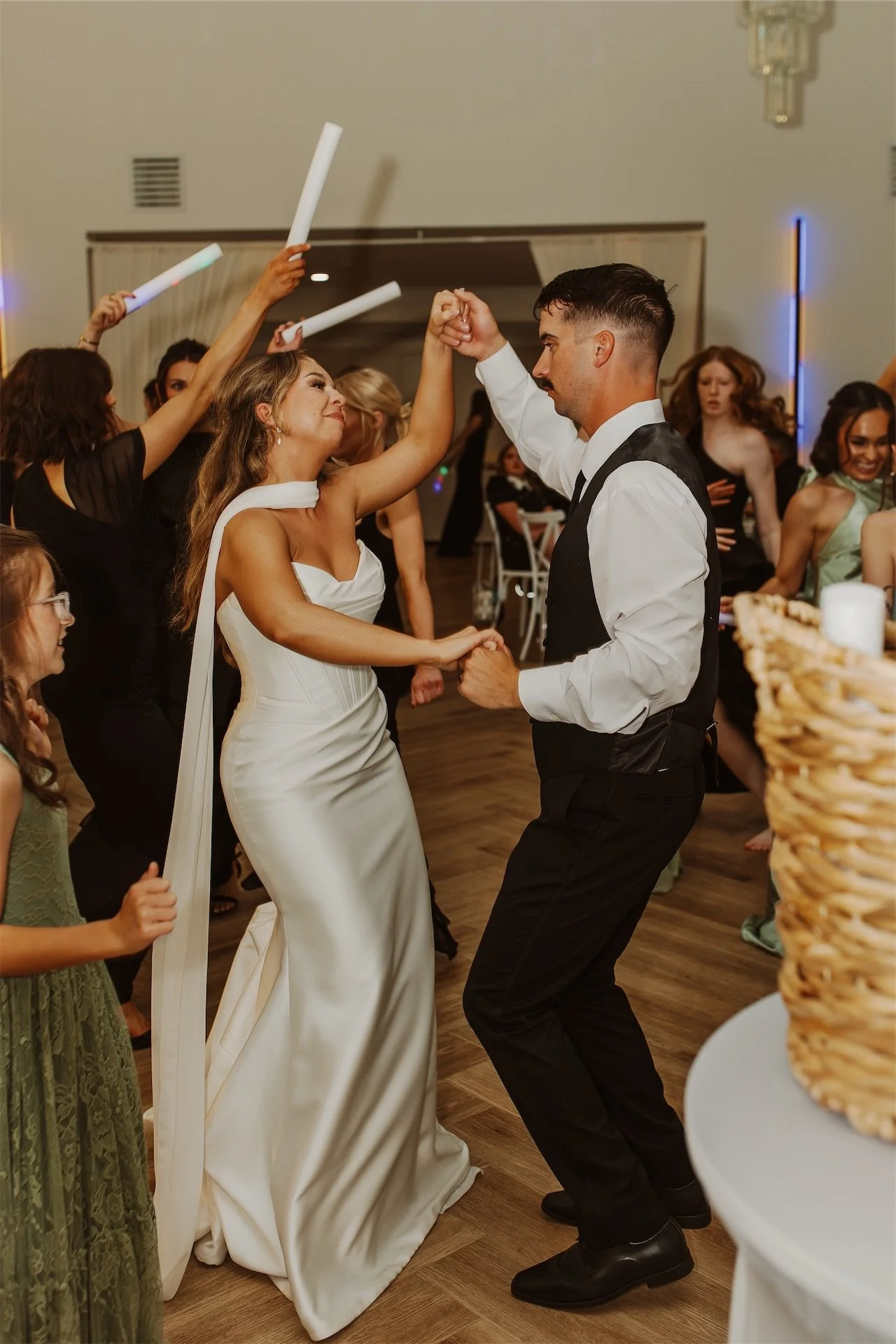 Bride and groom dancing together as guests cheer with glow sticks at reception