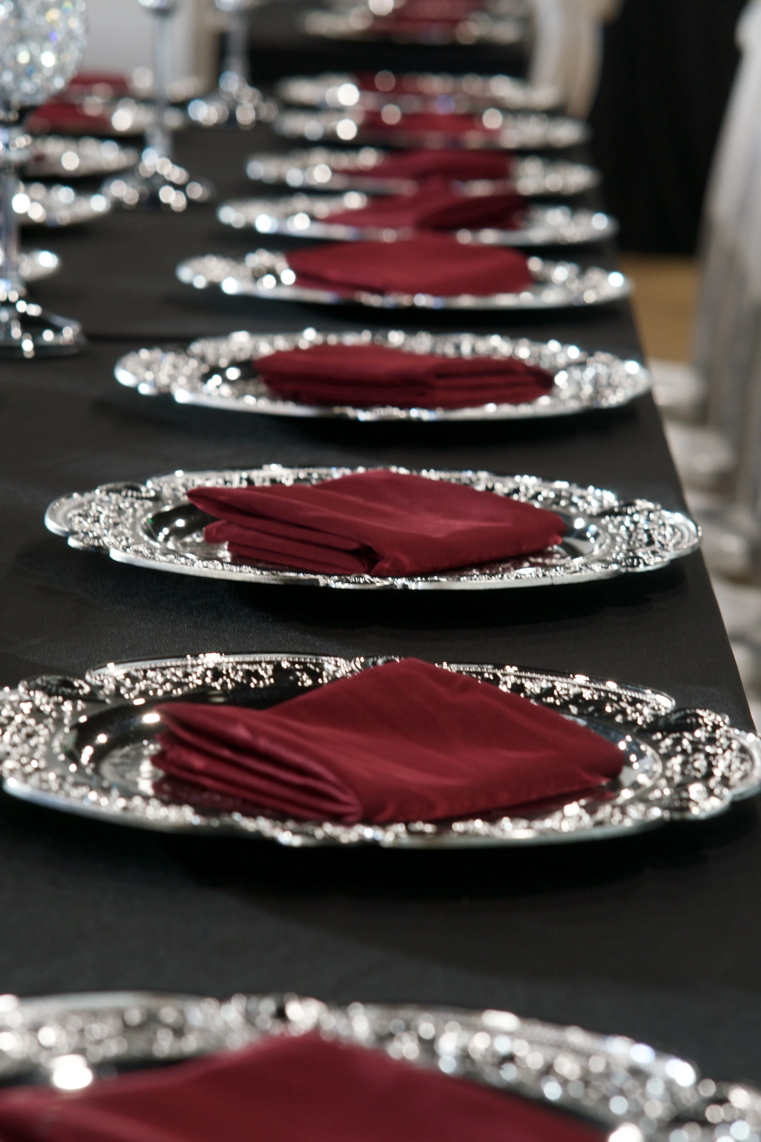 long reception table set with crystal goblets and burgundy napkin place settings