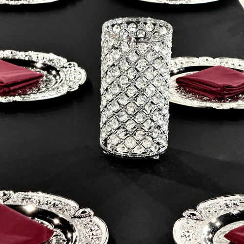close up of a crystal beaded cylinder centerpiece among silver charger place settings