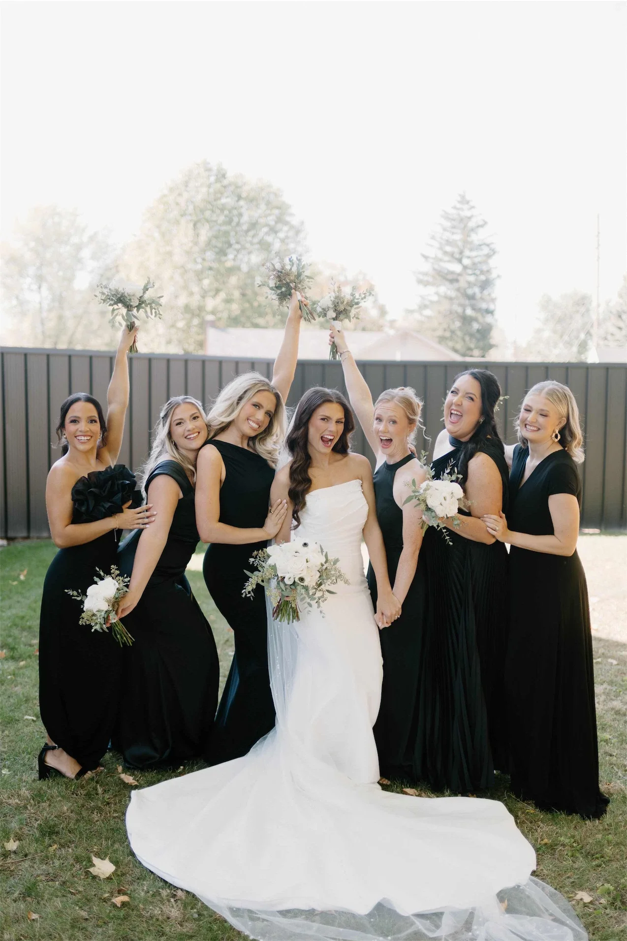 bridesmaids-cheering-bouquets-raised-black-dresses.webp
