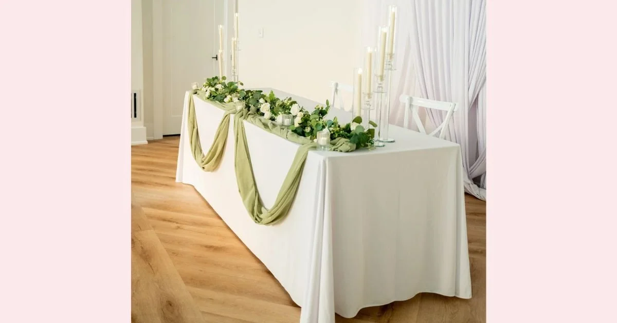 sweetheart table with sage green draping, ivory florals, and tall taper candles
